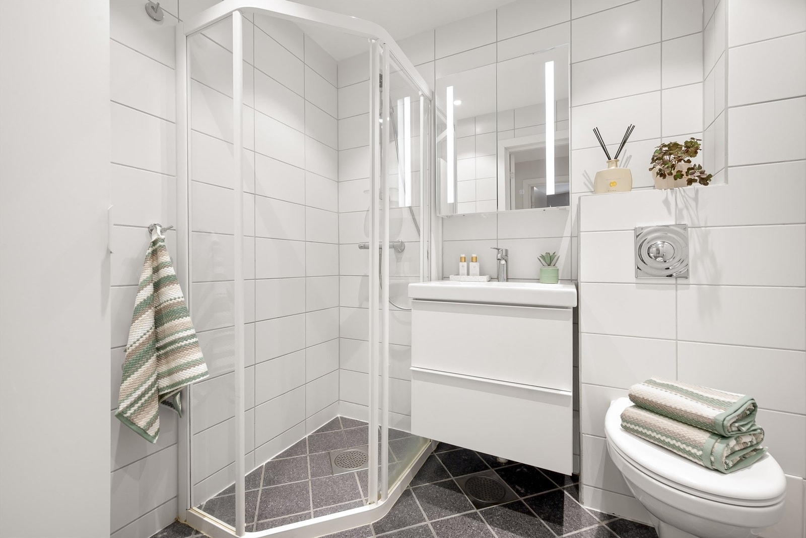 Pent og tidsriktig baderom med lyse fliser på vegg og mørke gulvfliser med varme under. Vegghengt toalett. Foto: Martine Eren Jacobsen. Galleribilde