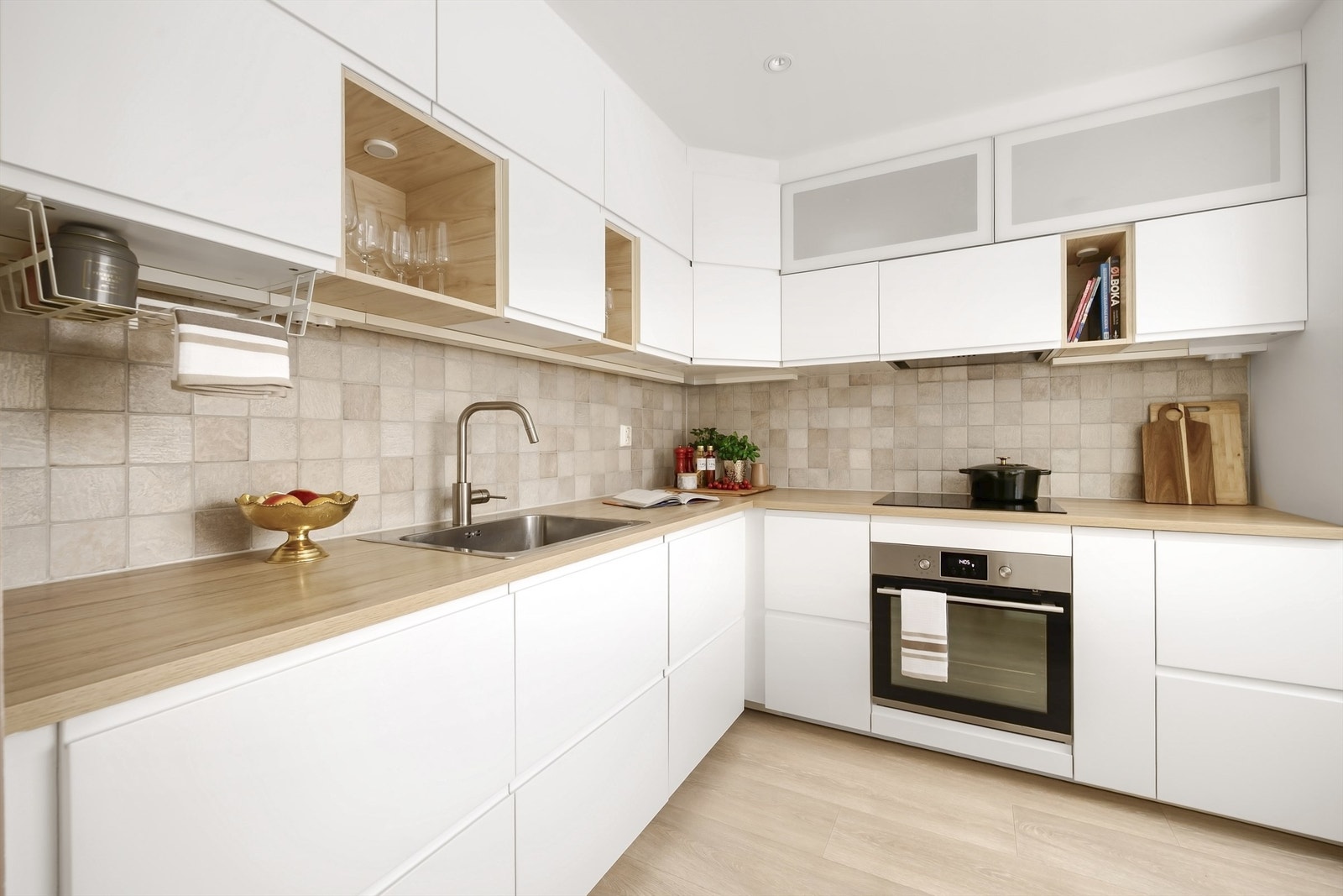 Stilrent og funksjonelt kjøkken fra IKEA med glatte fronter og laminert benkeplate. Benkeplaten har nedfelt oppvaskkum i rustfritt stål.
Kjøkkenet har fliser mellom benkeplate og overskap, overskapsbelysning og stikkontakter, Galleribilde