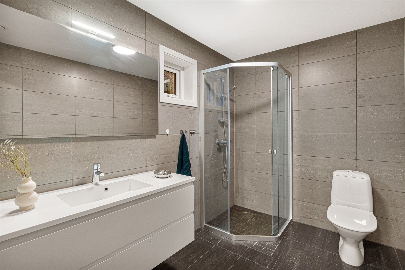 Badet i 1. etasje er tilsvarende som det i underetasjen og fremstår som tidløst og funksjonelt. Badet er innredet med vask i seksjon, dusj og toalett. Galleribilde