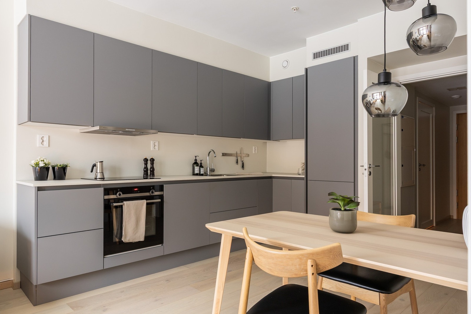 Smakfullt kjøkken med glatte, grå fronter og integrerte håndtak. Benkeplaten er i laminat med nedfelt stålkum. Galleribilde