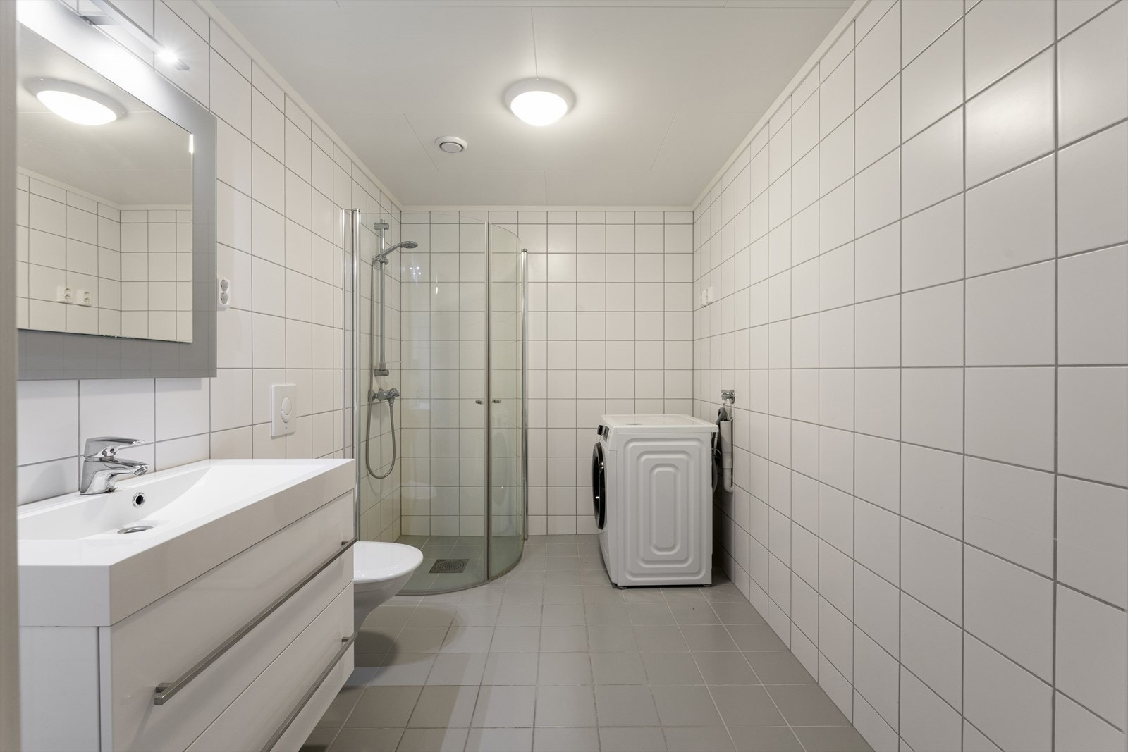 Baderommet er romslig og stilrent innredet med grå fliser på gulvet og hvite fliser på vegg. I gulvet har man også varmekabler for ekstra komfort. Galleribilde