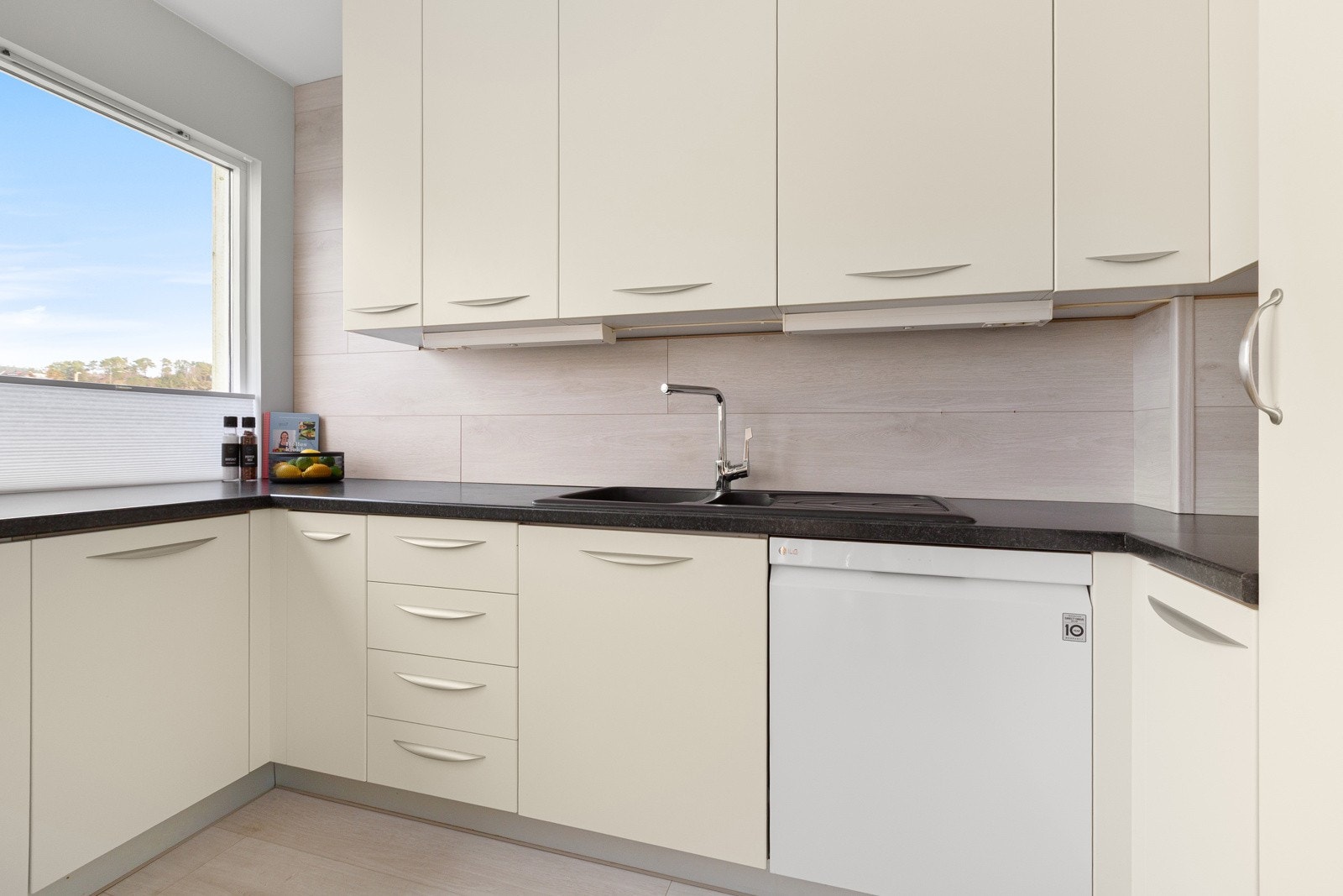 Lyst kjøkken med integrerte hvitevarer som platetopp, komfyr og kjøleskap, ellers er det frittstående oppvaskmaskin. Galleribilde