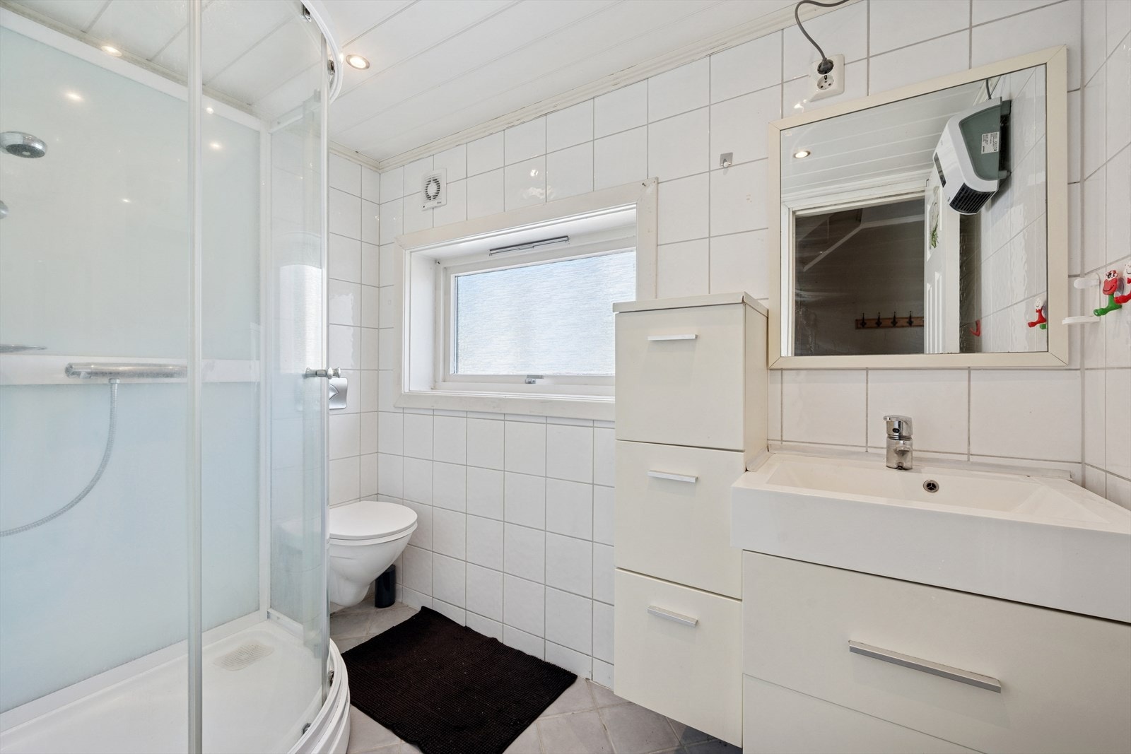 Pent flislagt bad med vegghengt klosett, dusjkabinett og servant med innredning. Galleribilde