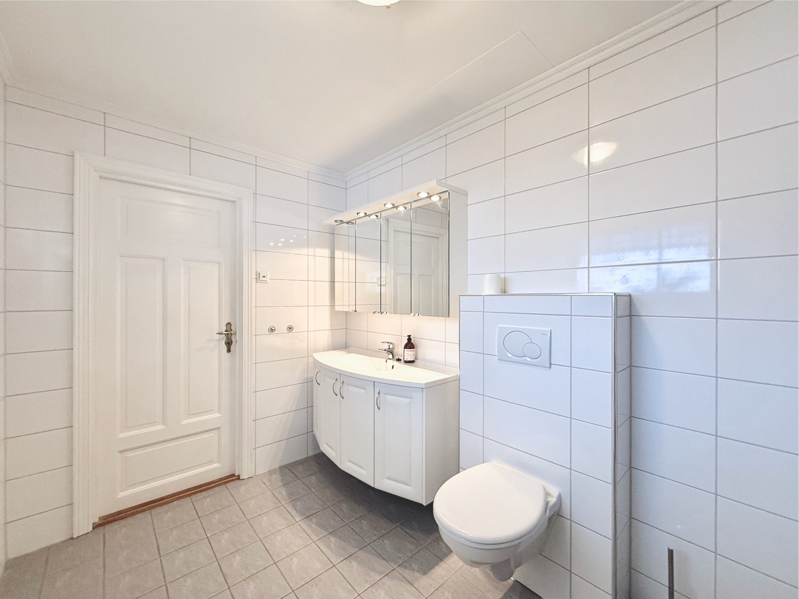 Flislagt bad med vegghengt toalett, underskap og speil Galleribilde