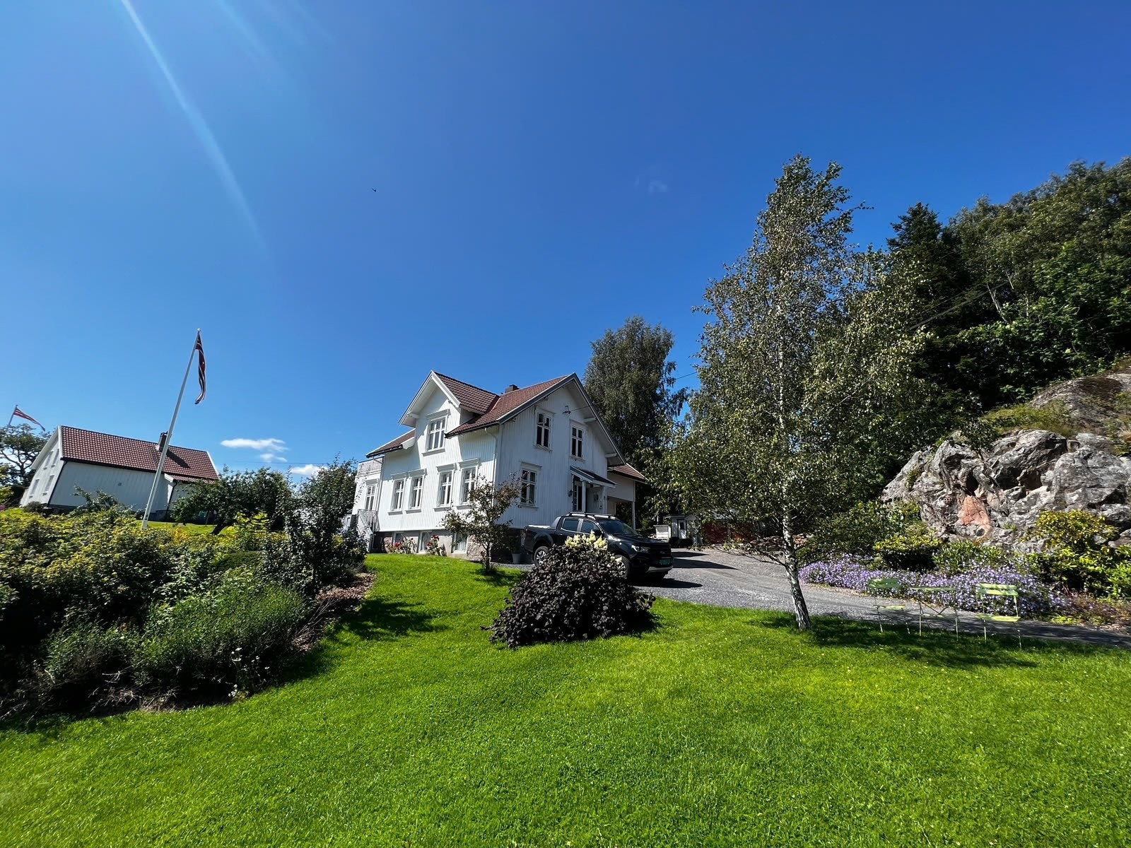 Sommerbilde av eiendommen med opparbeidet hage og solrik tomt Galleribilde