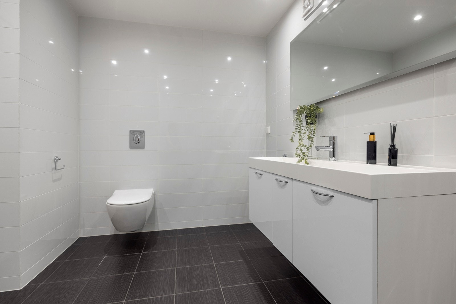 Badet har store blanke flisene gir et moderne preg samt rikelig av oppbevaringsplass Galleribilde