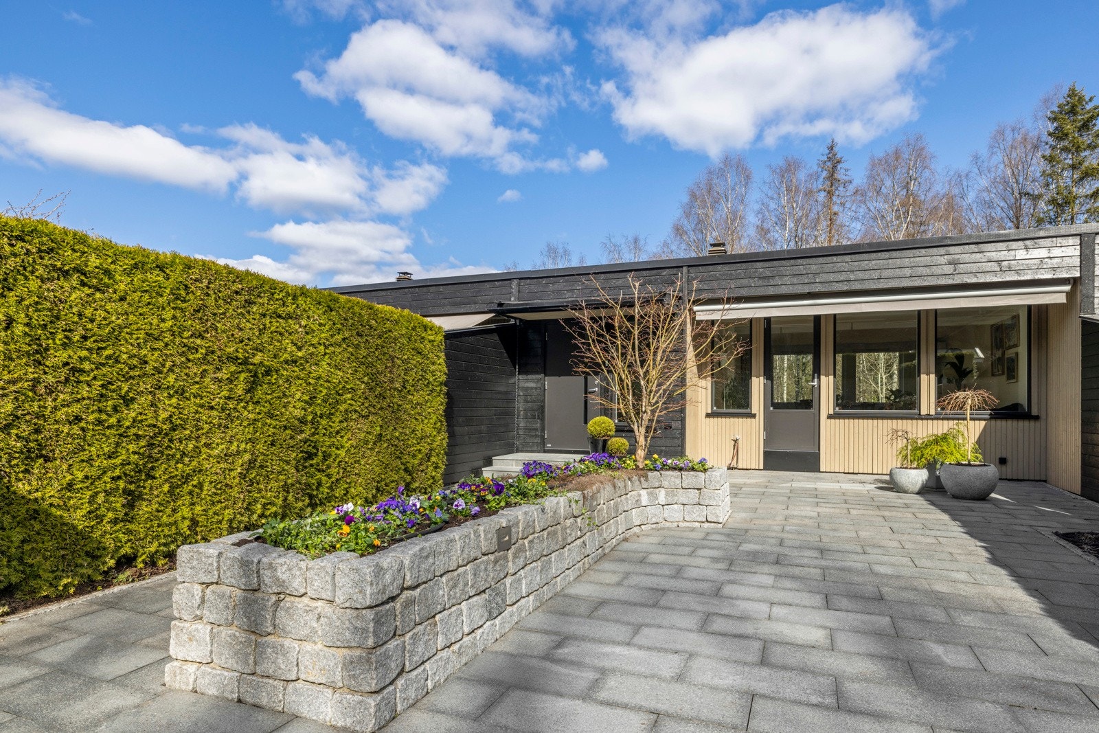 Eiendommen har en flott opparbeidet gårdsplass med blomsterbedd, granittheller og Tujahekk på sommeren Galleribilde