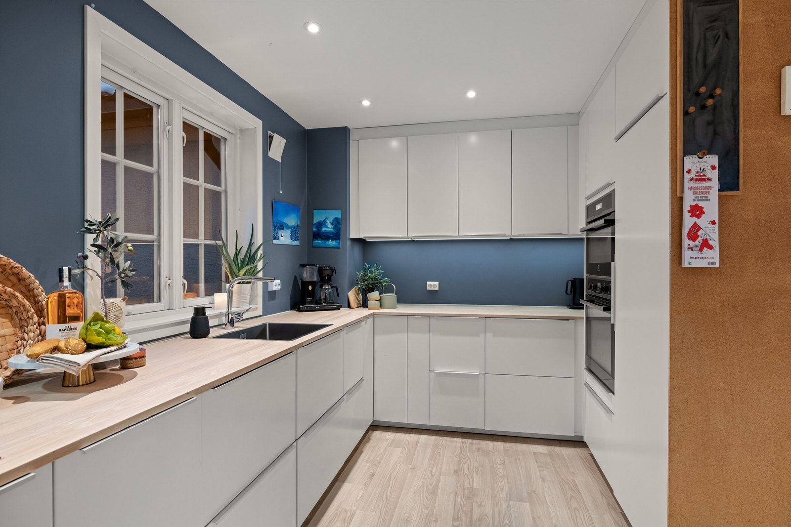 Kjøkkeninnredningen har hvite glatte fronter og integrerte hvitevarer, inkludert ovner i høyskap. Det er også en støvsuger i sokkelen under høyskapet for å fjerne smuler på kjøkkengulvet. Galleribilde