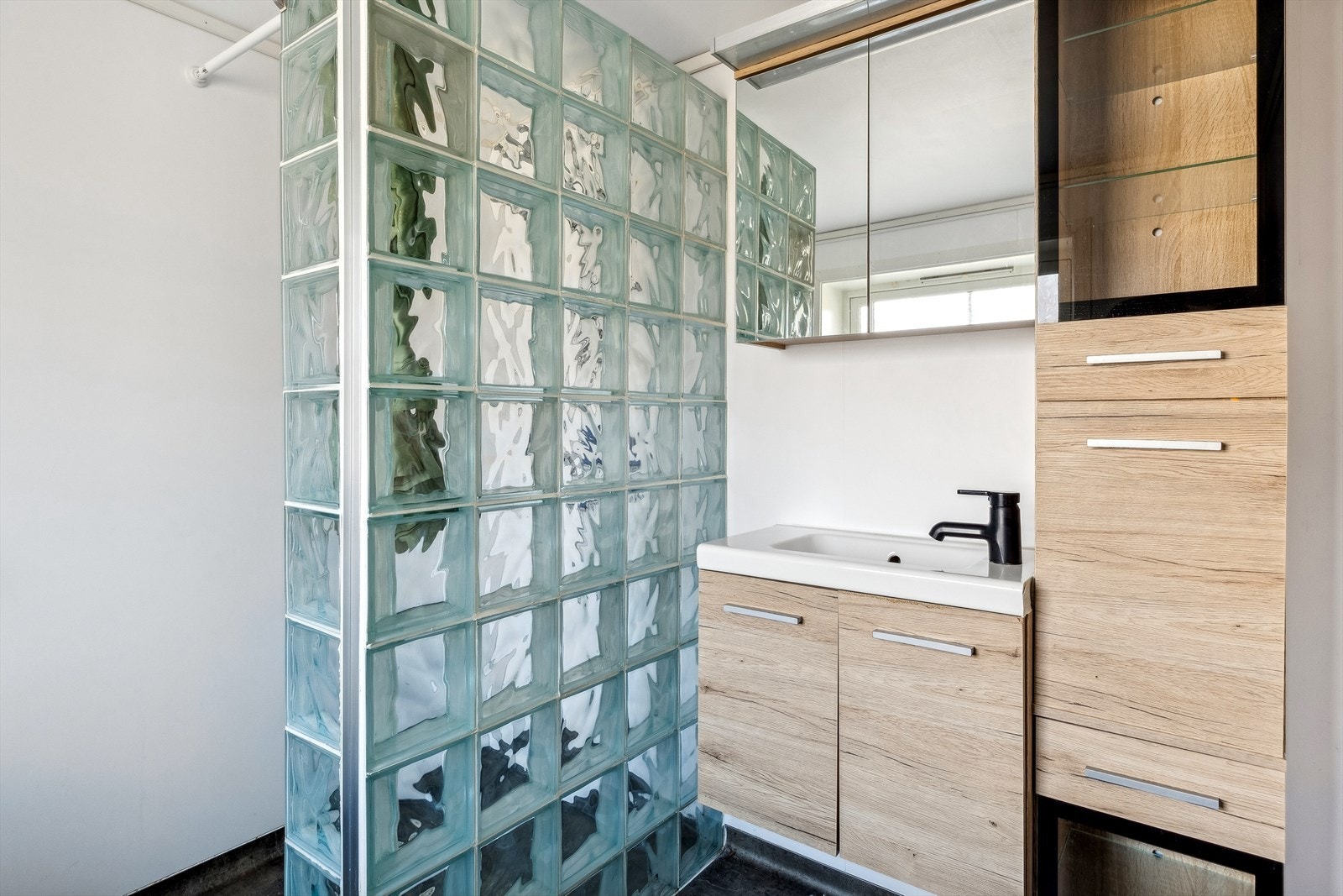 Badet har dusjvegger av glass, gulvmontert toalett, innredning med servant samt opplegg for vaskemaskin. Galleribilde