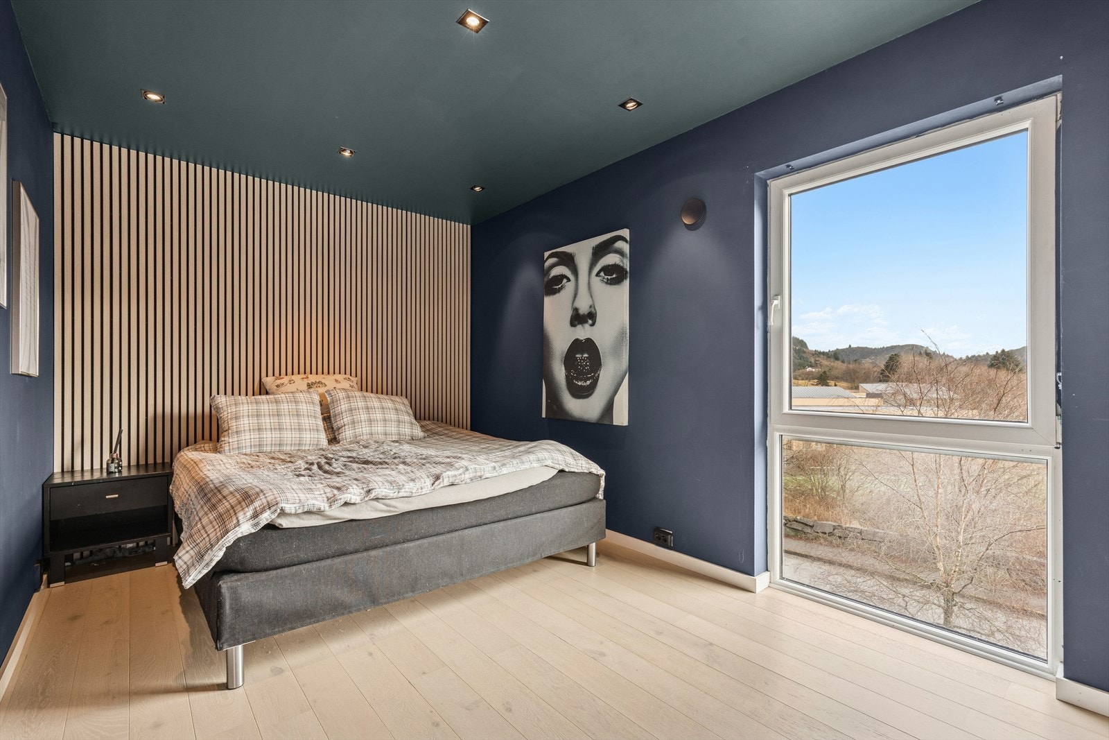 Romslig soverom på hele 12,6 m², med store vinduer som gir rikelig naturlig lys og flott utsyn. Rommet har moderne spotbelysning i taket, lekker spilevegg som gir et eksklusivt uttrykk, samt lys parkett som skaper en varm og behagelig atmosfære. Galleribilde