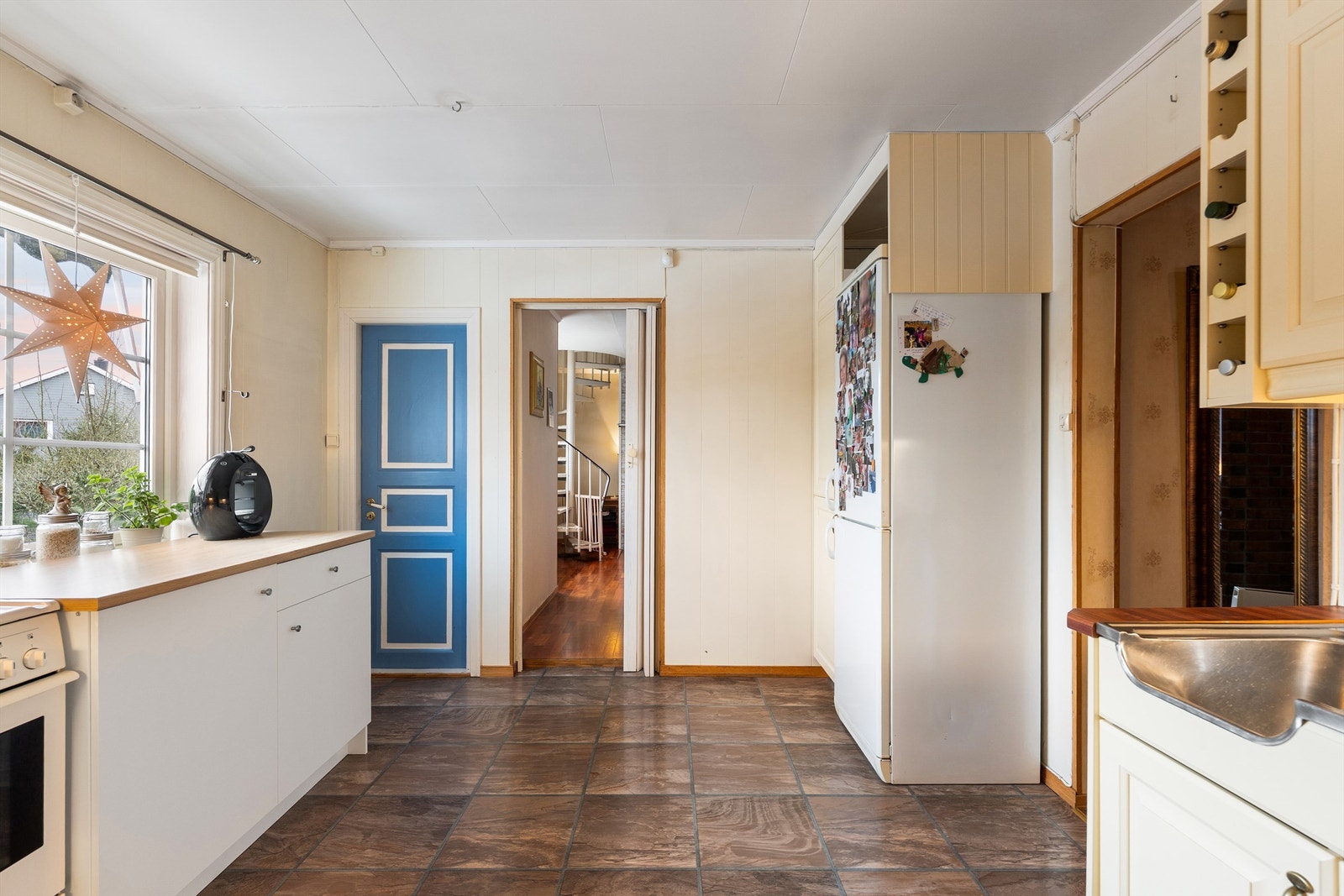 Bak blå dør leder trapp ned til vaskerom i kjelleren. Innenfor kjøkkenet finnes etasjens soverom. Galleribilde