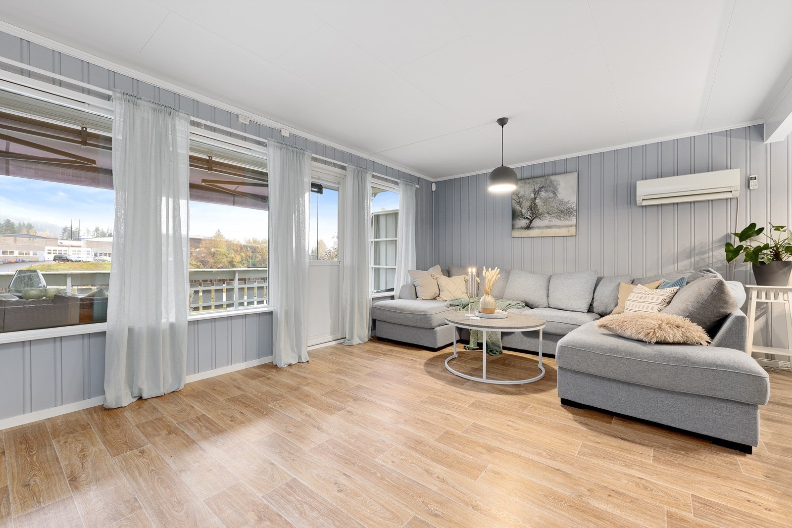 Stuen er lys og innbydende med lys 1-stavs laminat på gulv og panel vegger malt i et lyst fargepalett. Galleribilde