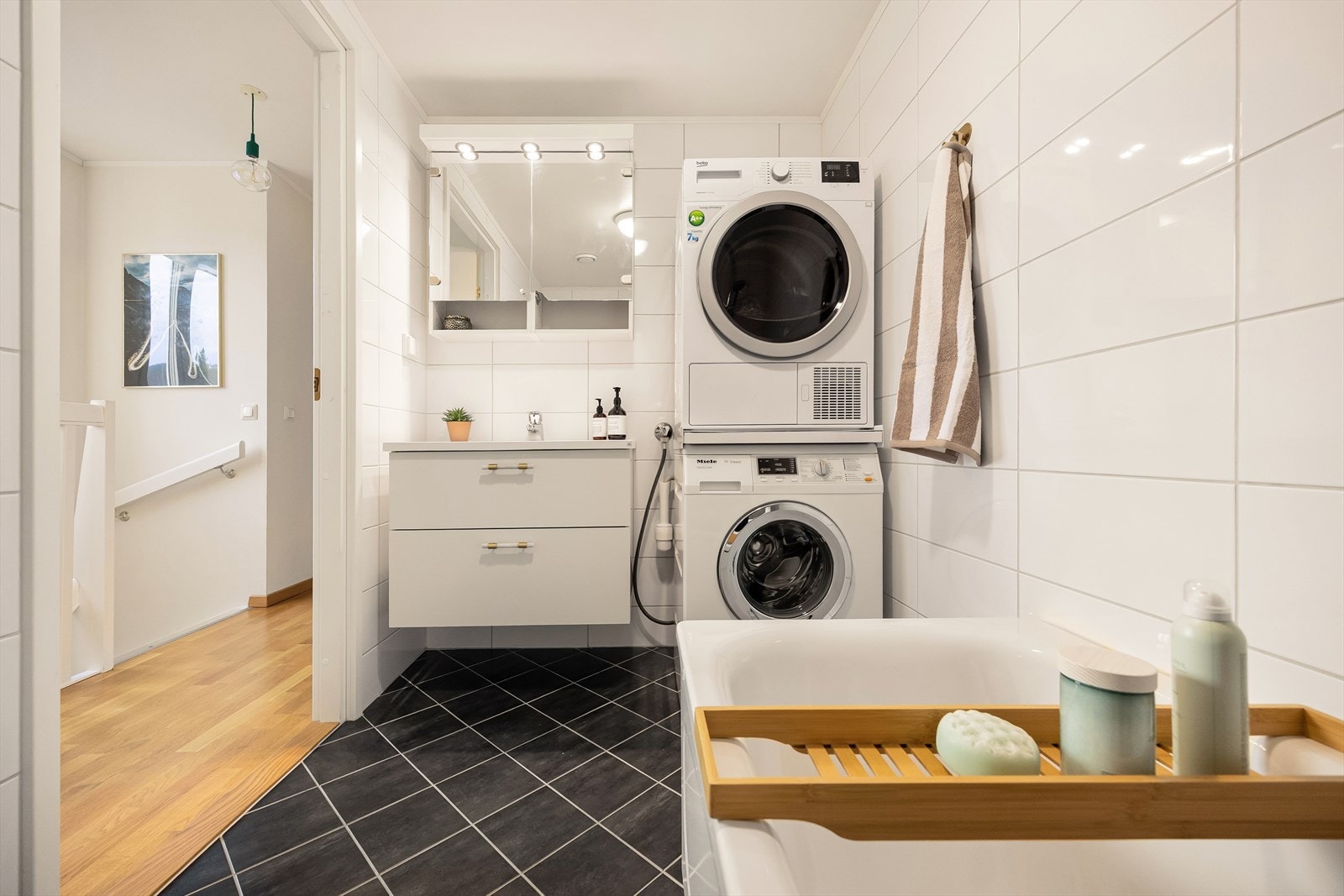 Pent flislagt bad med opplegg for vaskesøyle, servant med innredning, vegghengt toalett, badekar og dusjgarnityr. Galleribilde