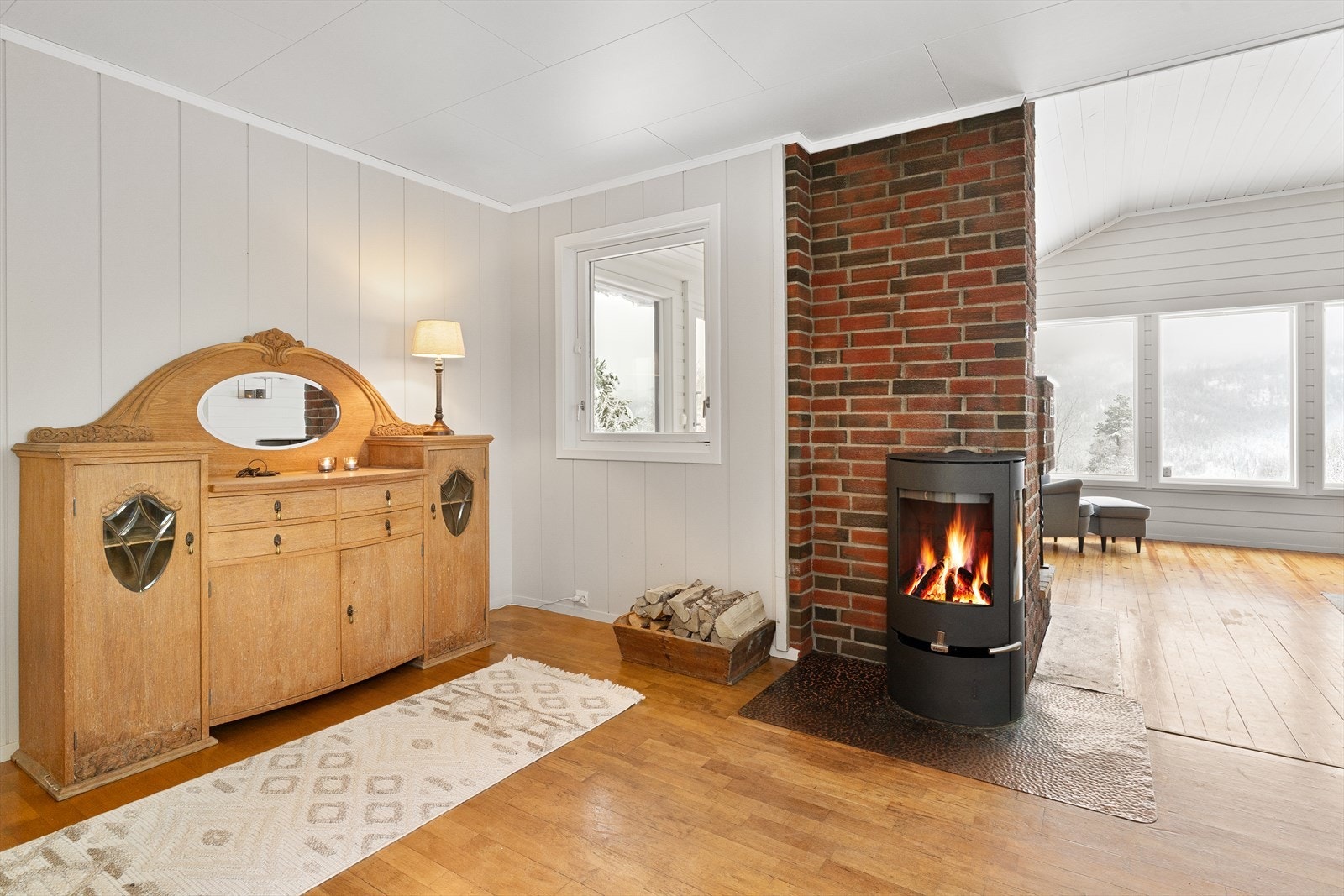 Stuen fremstår lys og koselig med lyst panel på vegger, furu gulv og store vindusflater som bringer med seg mye naturlig lys inn. Galleribilde