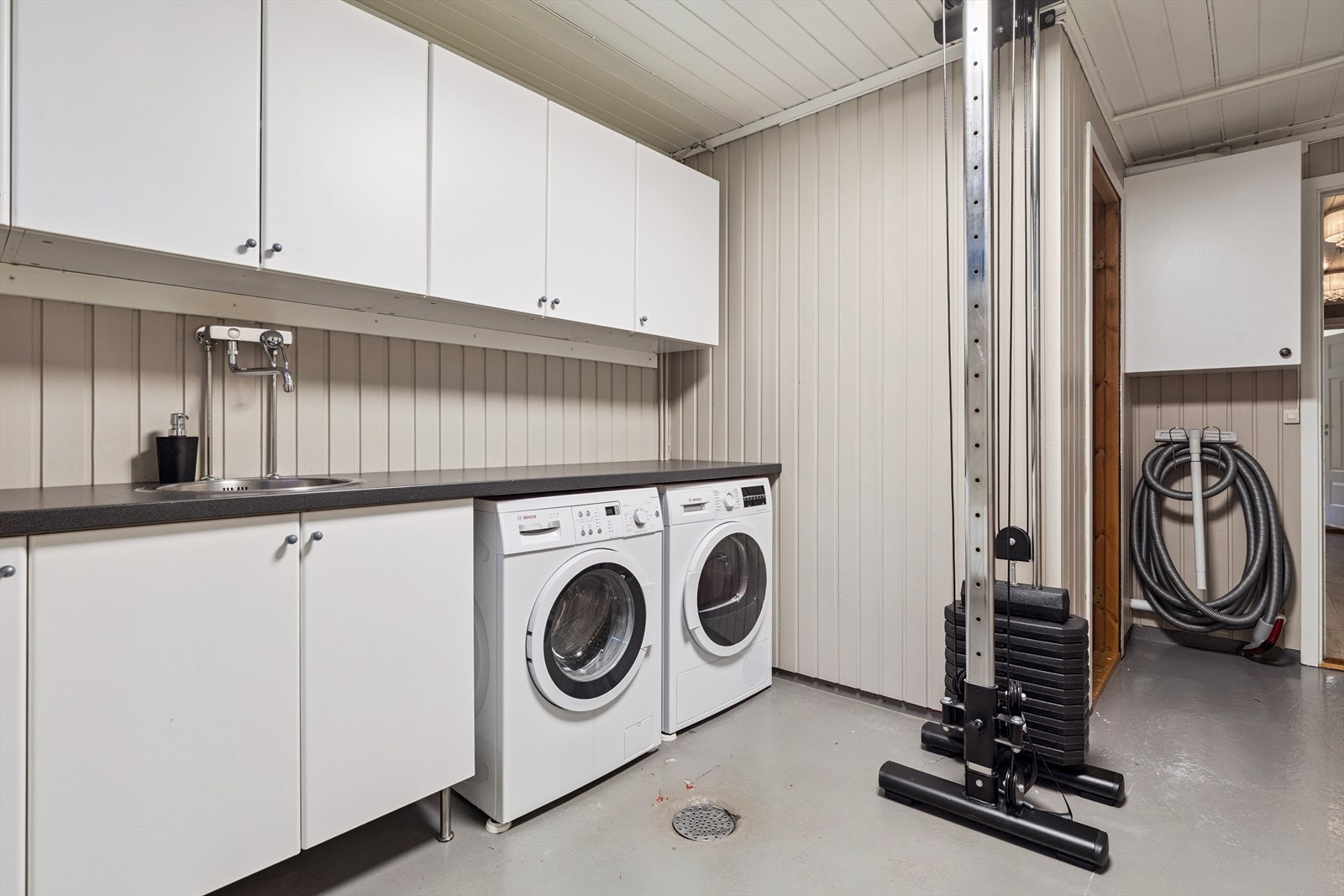 Et separat og funksjonelt vaskerom med benkeinnredning, vask og opplegg for vaskemaskin. Galleribilde