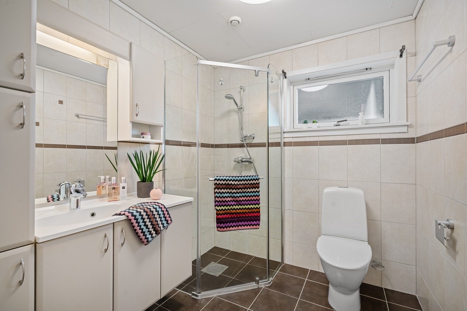 Badet i hovedetasjen er flislagt på gulv og vegger. Det har nedfelt servant i skapseksjon som gir god oppbevaringsplass, samt hjørnedusj og toalett. Et funksjonelt og praktisk bad til daglig bruk. Galleribilde