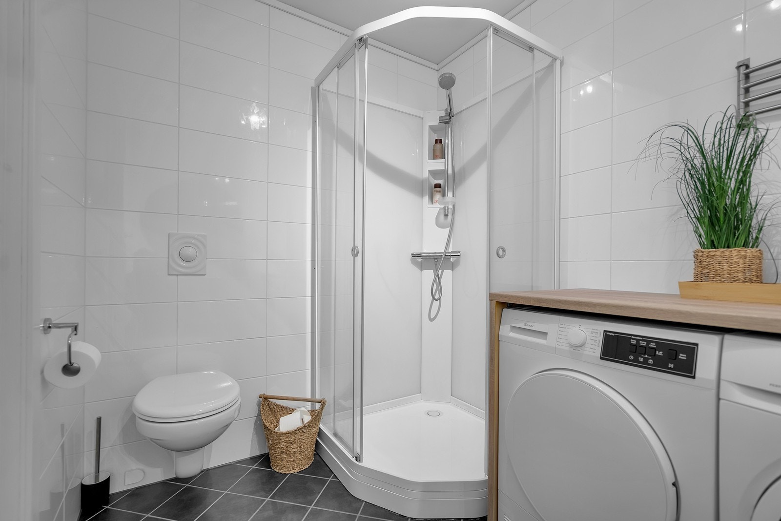 Badet er utstyrt med vegghengt toalett, dusjkabinett, servant og opplegg for vaskemaskin Galleribilde