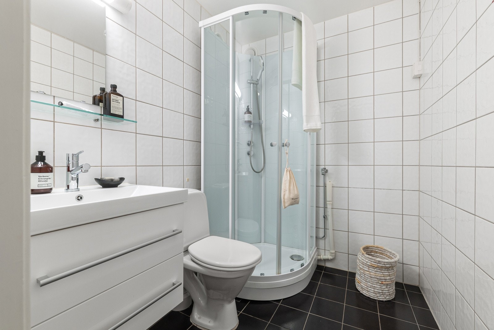 Eldre flislagt bad innredet med dusjkabinett, gulvmontert toalett, servantskap og opplegg for vaskemaskin. Galleribilde