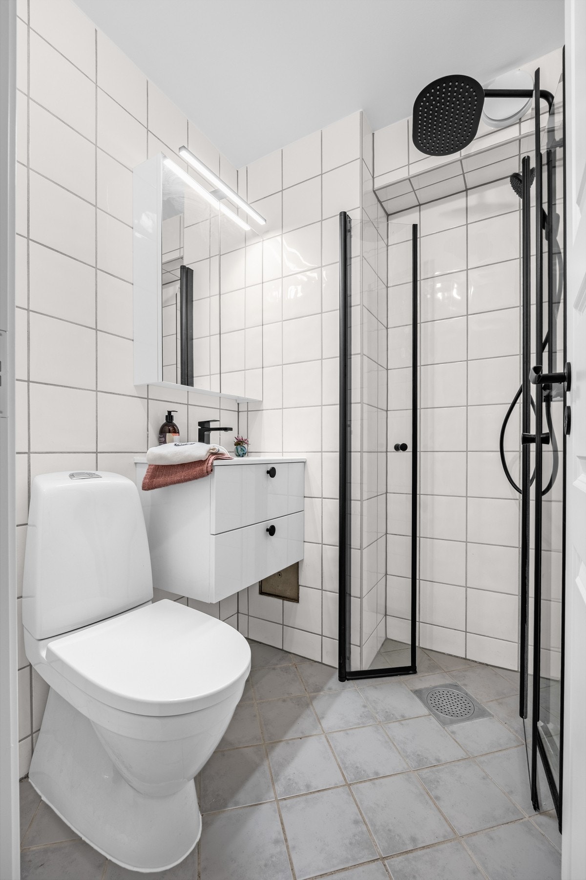 Lyst bad med flislagte flater, sorte detaljer og regndusj som gir et tidløst og gjennomført preg. Galleribilde