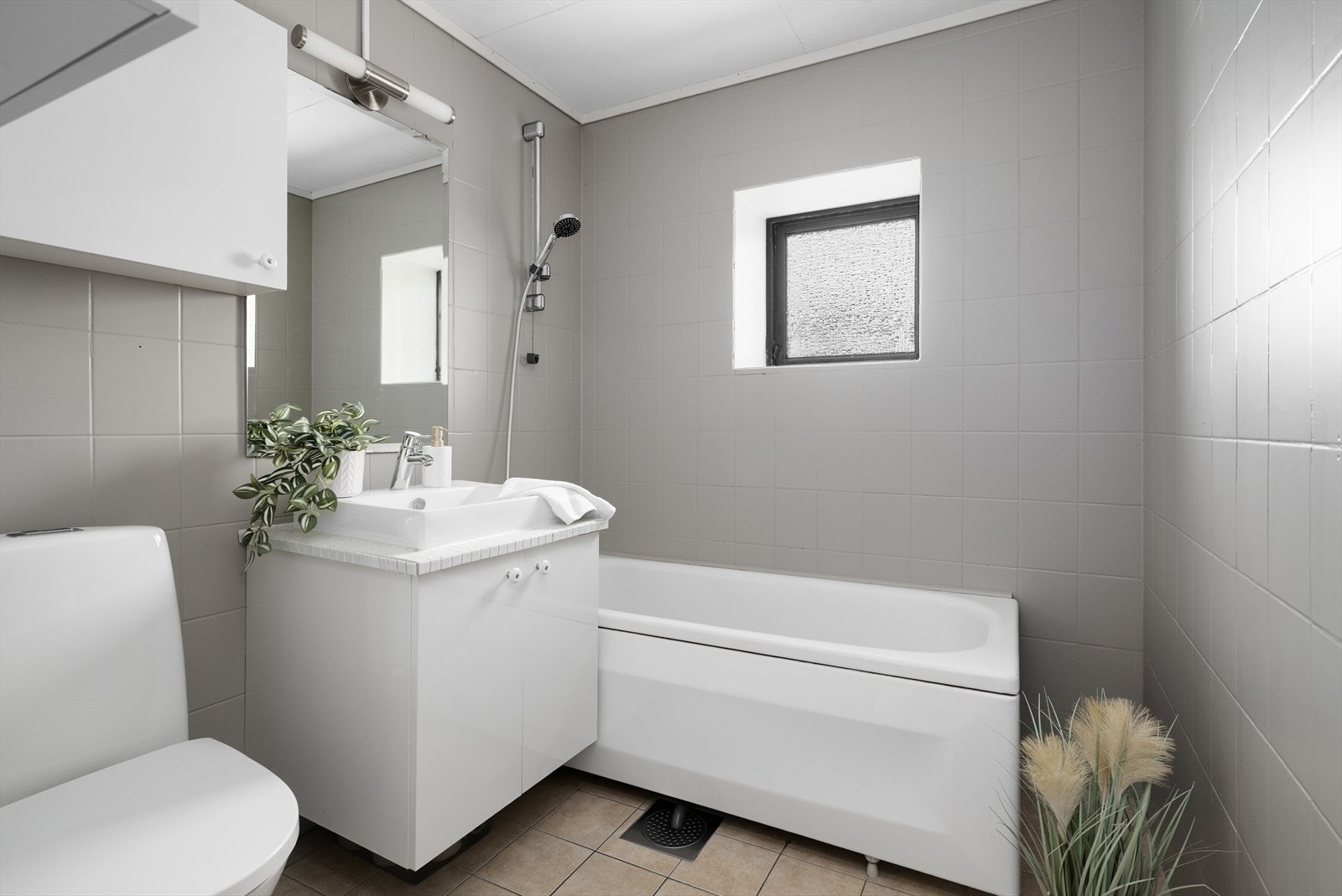 Flislagt bad av eldre standard med varmekabler i gulv, badekar og servantinnredning med overliggende vask. Nytt, gulvmontert toalett fra 2025. Galleribilde