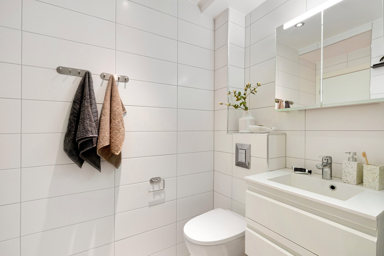 Innredet med veggmontert toalett, dusjvegg/dører i herdet glass, speilskap med integrert belysning, baderomsinnredning med malte fronter og heldekkende servant. Galleribilde