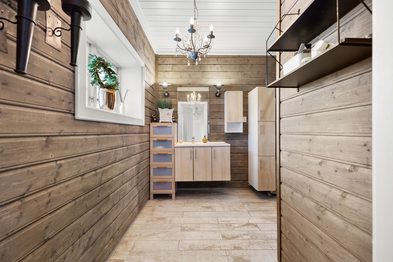 Bad med liggende beiset kledning på vegger og fliser på gulv. Badet har servantinnredning med servant og armatur og dusjkabinett. Galleribilde