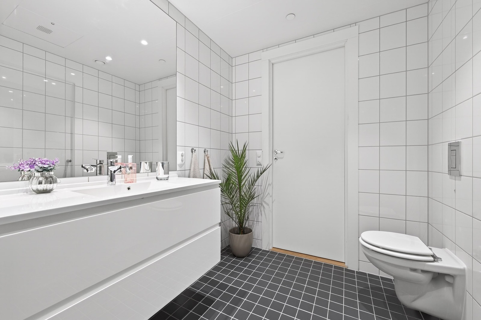 Videre er badet innredet med servant med speil og sideskap, vegghengt toalett og dusjhjørne. Galleribilde