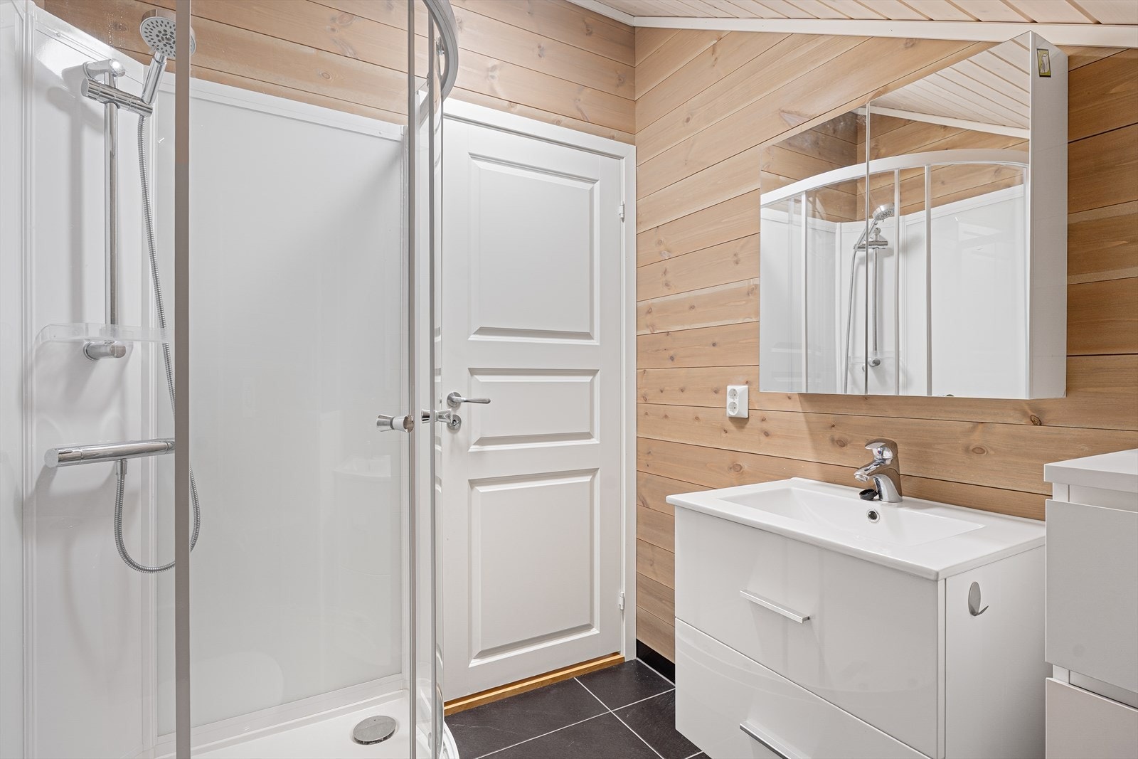 Bad i loftsetasjen er innredet med dusjkabinett, gulvmontert toalett, veggskap med speifronter og baderomsinnredning med heldekkende servant. Galleribilde
