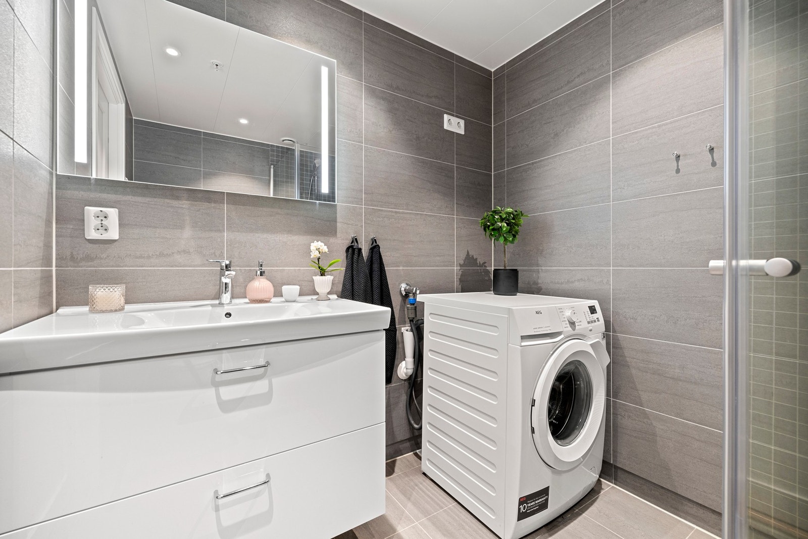 Her er det en lys og pen baderomsinnredning med servant og armatur, et romslig dusjhjørne med dusjarmatur, vegghengt toalett og opplegg for vaskemaskin. Galleribilde