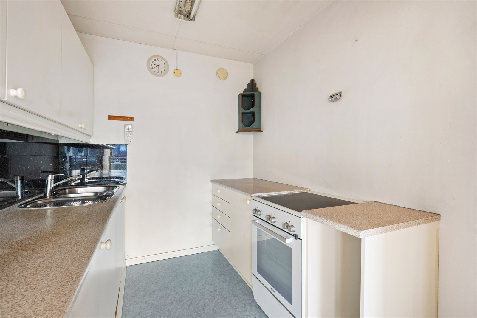 Eldre kjøkkeninnredning med glatte fronter. Benkeplaten er av laminat. Vinylbelegg på gulv. Galleribilde