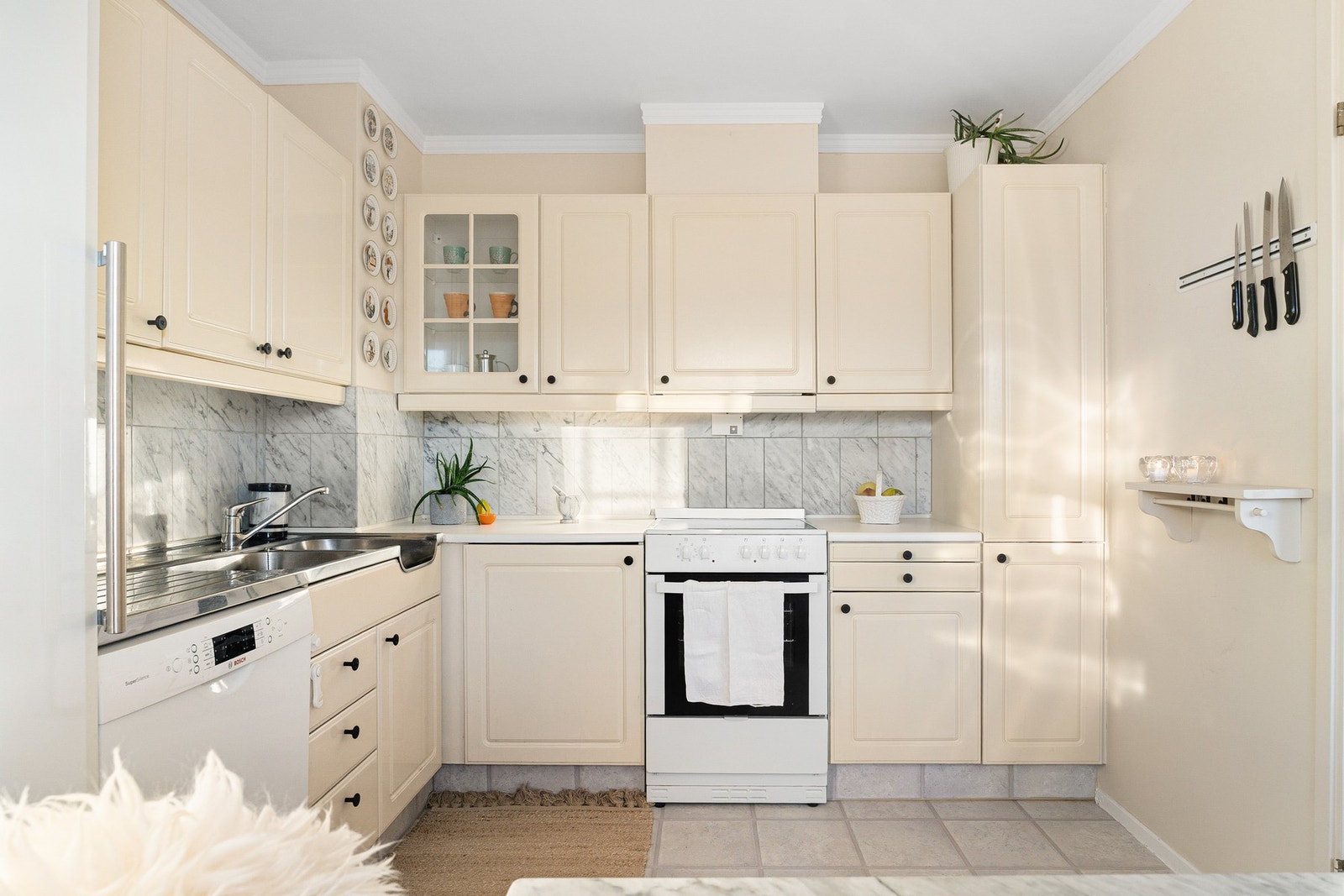 Sjarmerende kjøkken innredet med profilerte lakkerte fronter og laminert benkeplate. Mellom benkeplate og overskap er det marmorfliser. Galleribilde