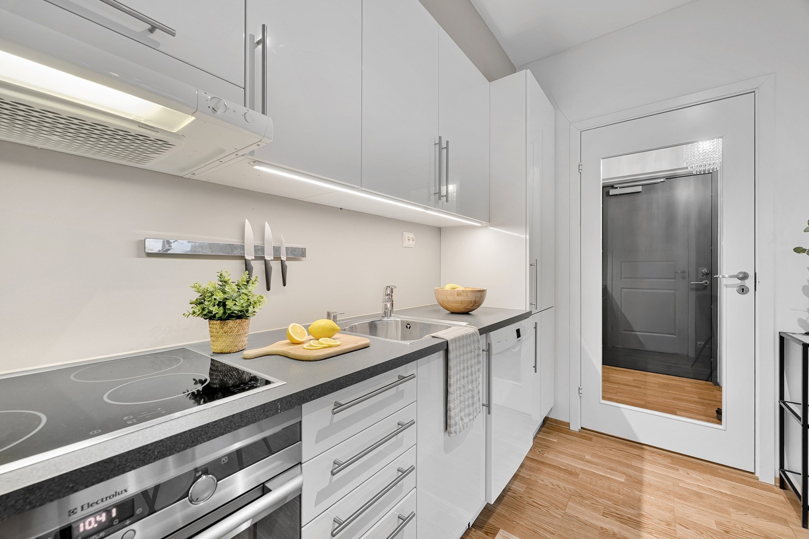 Kjøkken med kjøkkeninnredning i hvite, slette fronter og mørk benkeplate. Galleribilde