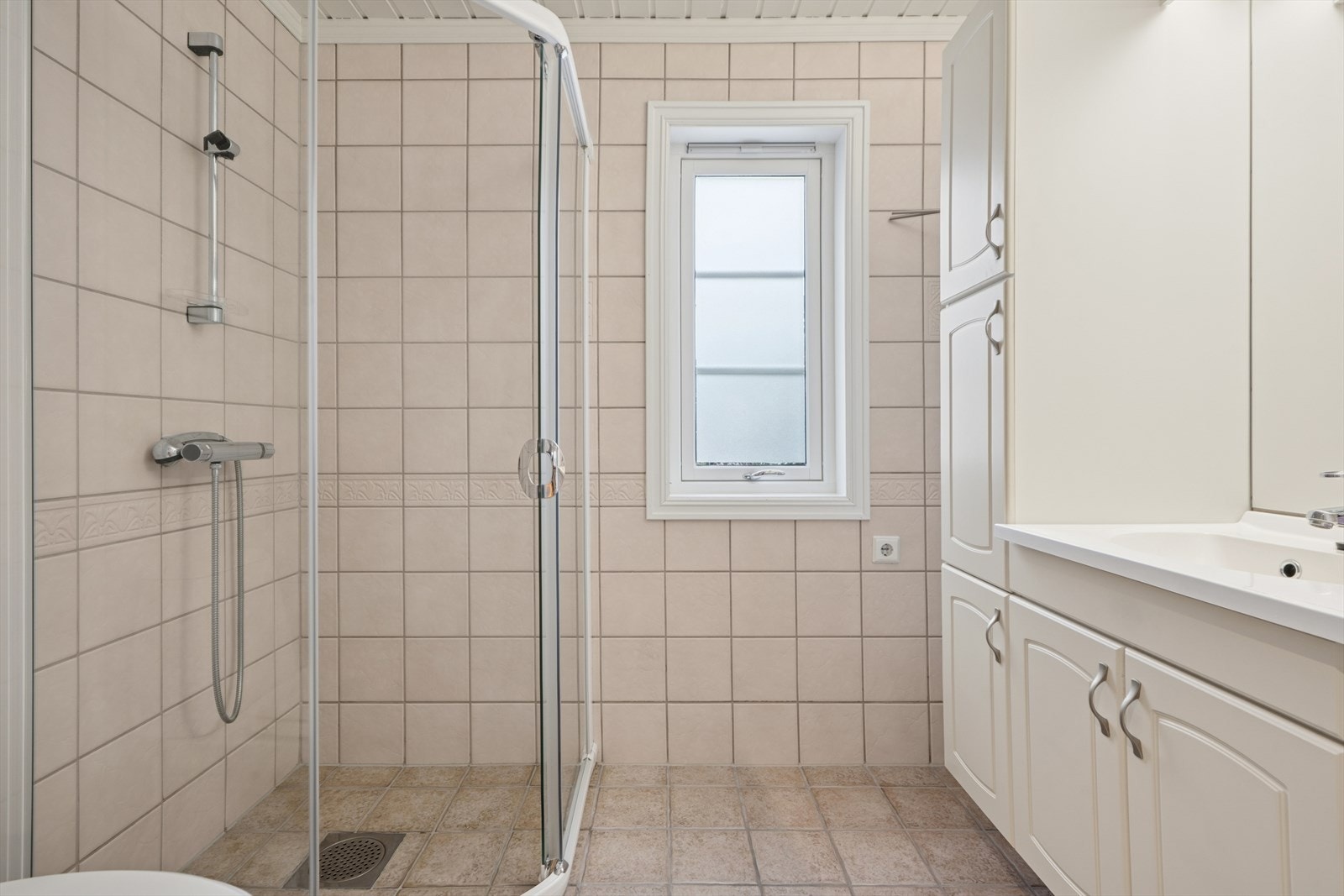 Flislagt bad i 1. etasjen med varmekabler i gulvet. Badet er innredet med toalett, dusjhjørne med dusjvegger og baderomsinnredning med servant og speil. Galleribilde