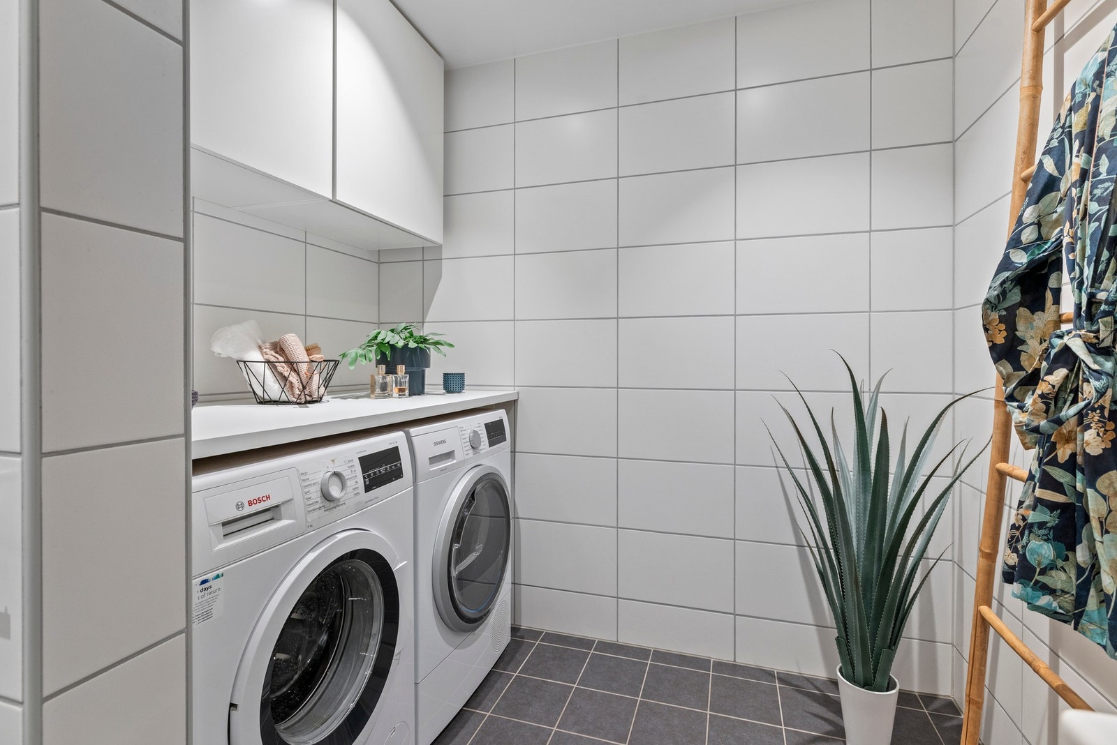 Innerst i rommet finner du en vaskesone med opplegg til vaskemaskin og tørketrommel, en praktisk benk og to skap Galleribilde