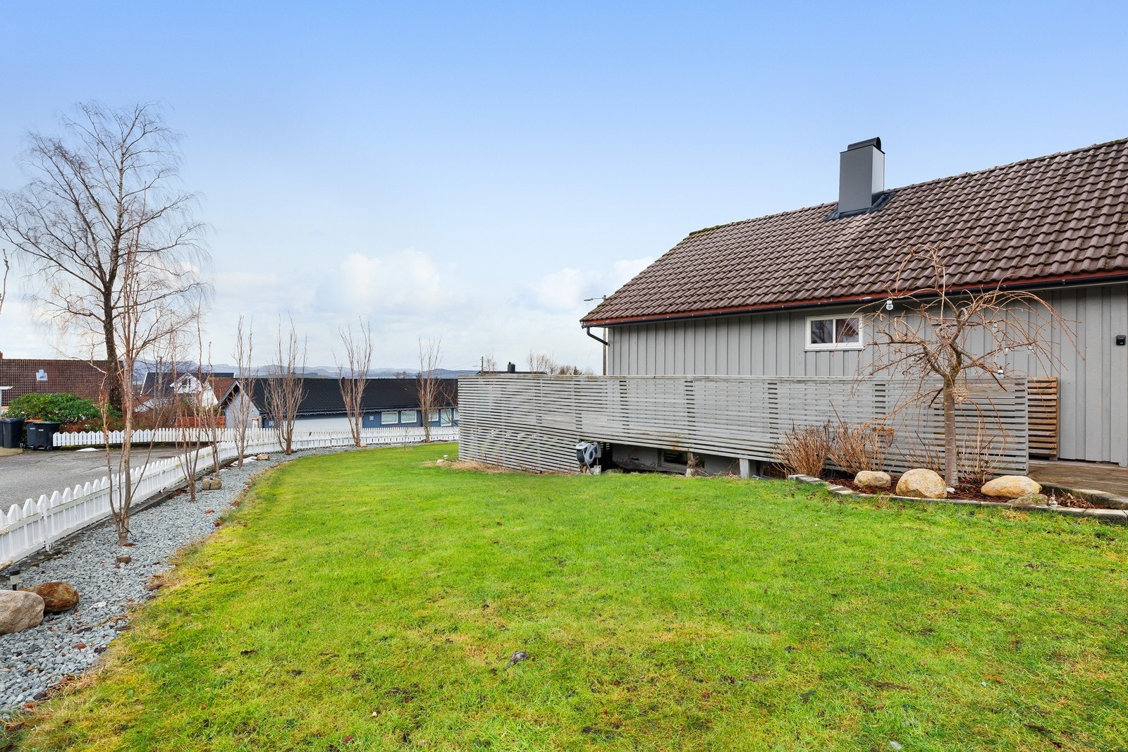 Hagen er rammet inn av hvitt gjerde, singelbed og trær. Fruktrær og bærbusker. Galleribilde