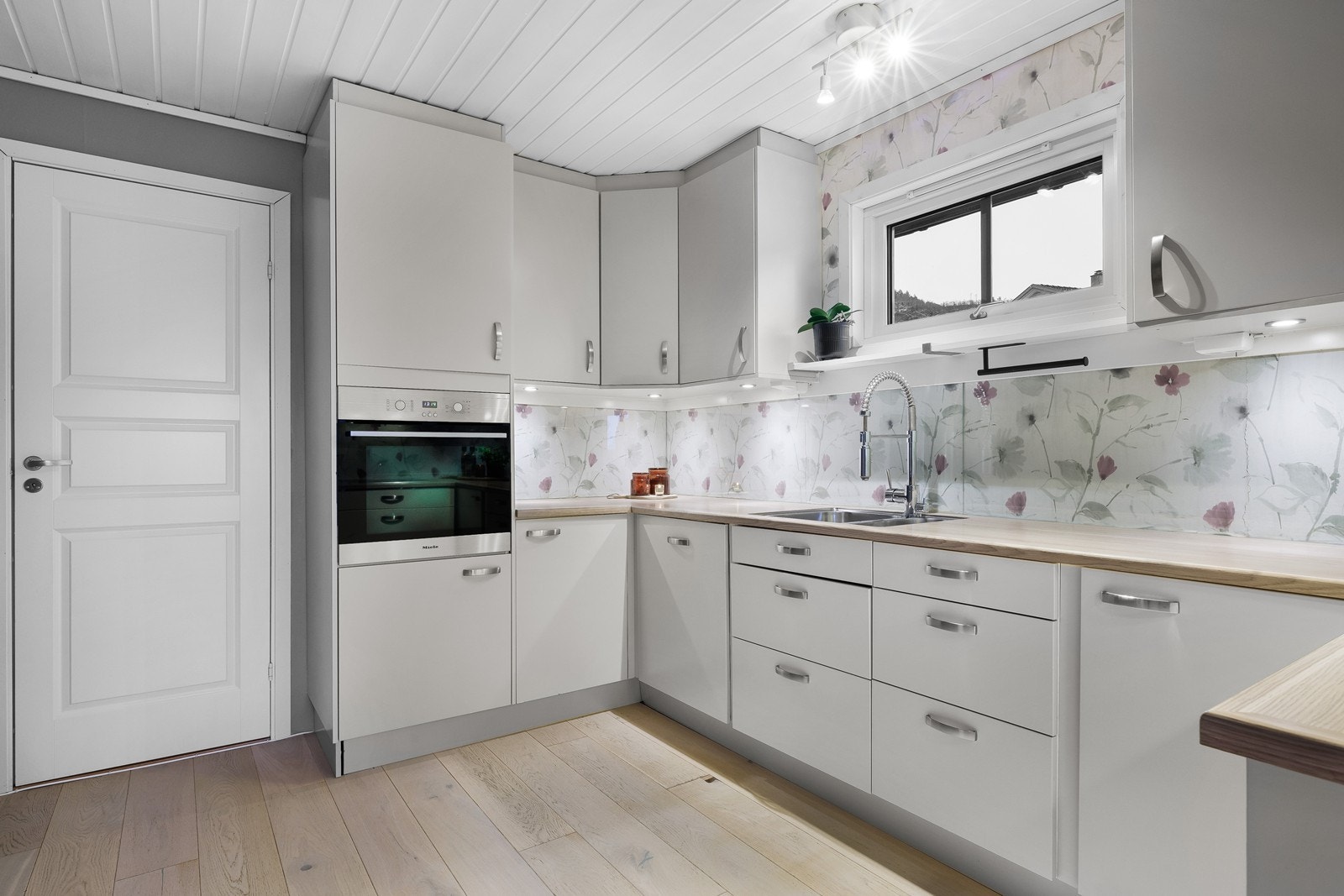 Lyst og tidsriktig kjøkken med dekorativ tapet og glassplate over benk. Galleribilde