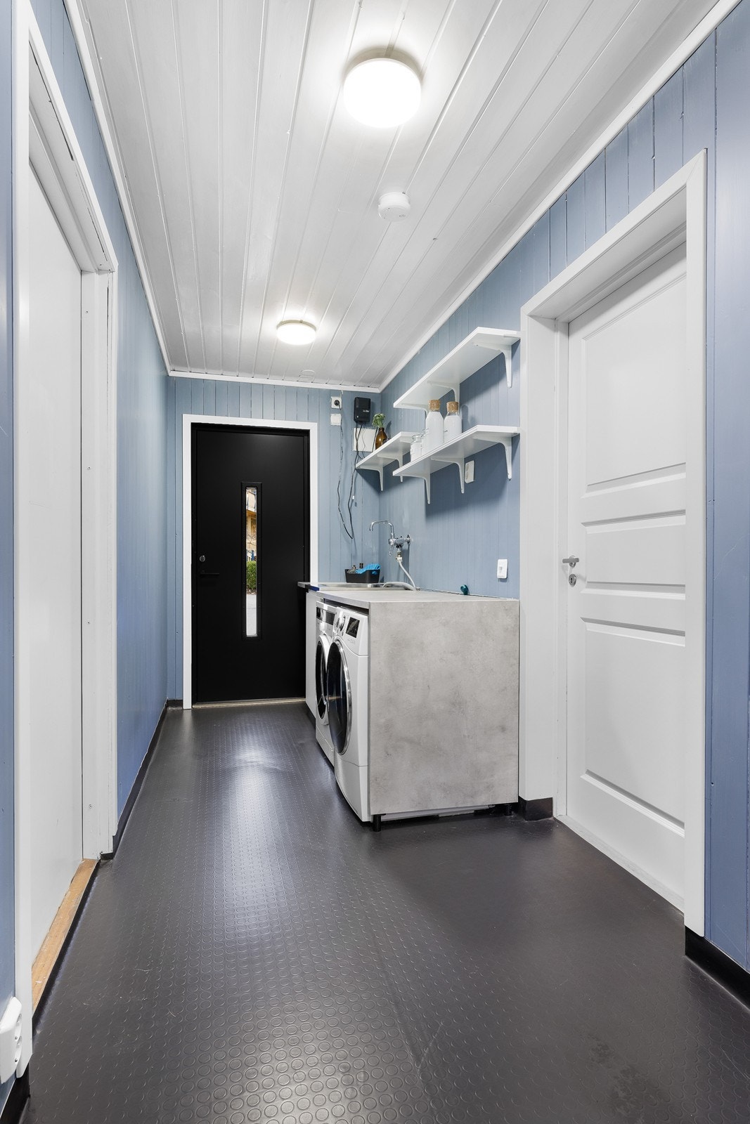 Gjennomført og funksjonelt vaskerom med flere adkomster. Praktisk rom med grovt gulvbelegg, benk og hyllesystem. Galleribilde