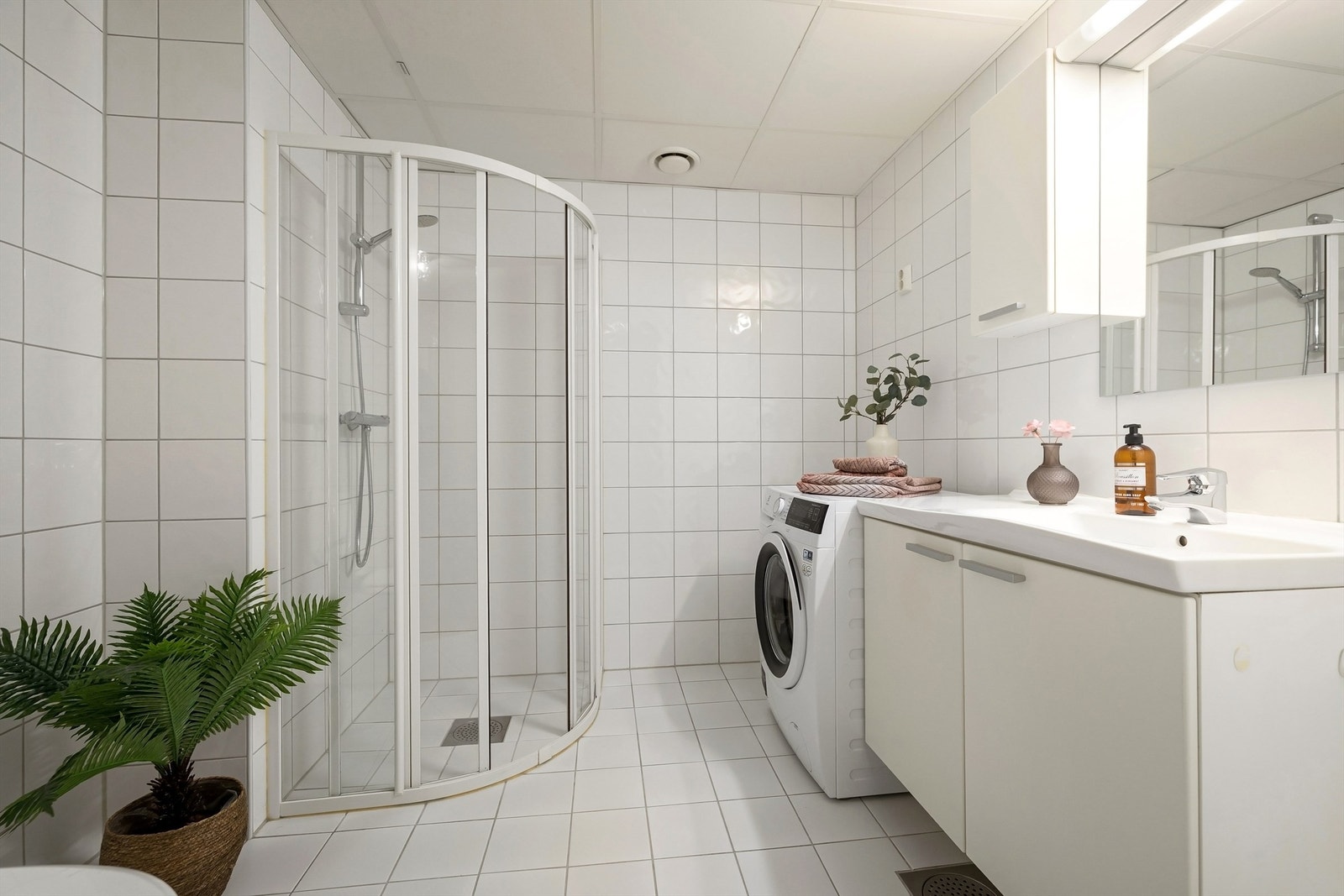 Pent baderom med hvite fliser på gulv og vegger samt gulvvarme. Opplegg for både vaskemaskin og tørketrommel Galleribilde