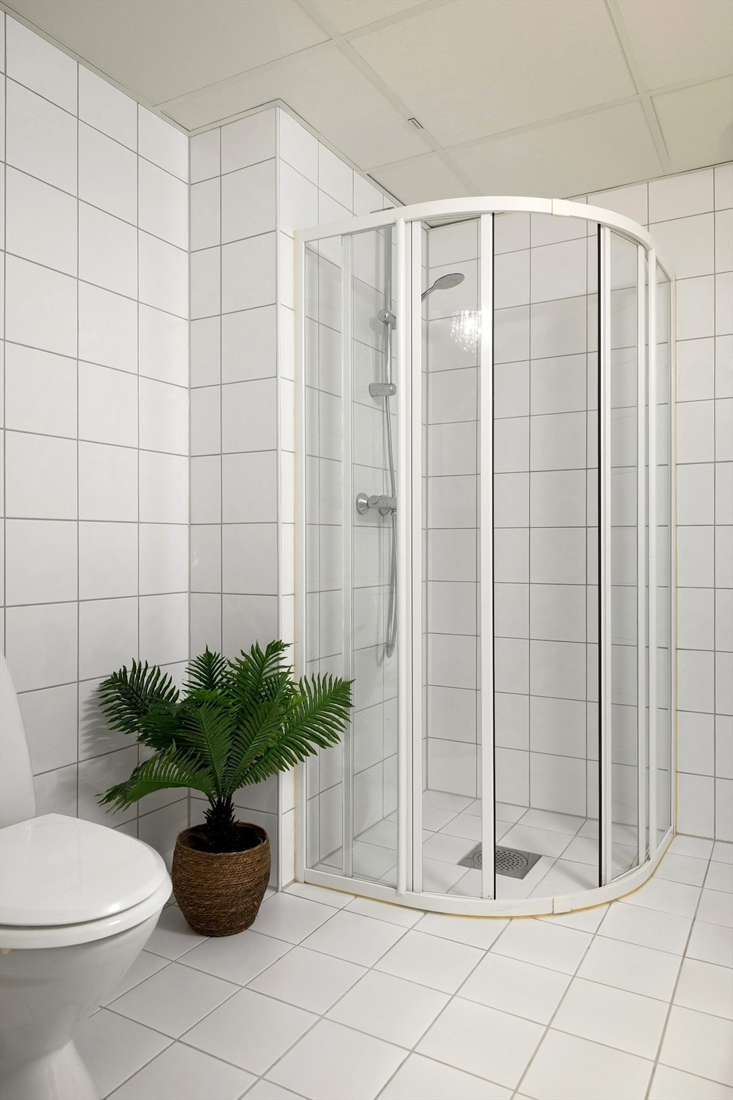 Badet er utstyrt med frittstående toalett, dusjhjørne med skyvedører, heldekkende servant med skapinnredning og speil med belysning over Galleribilde