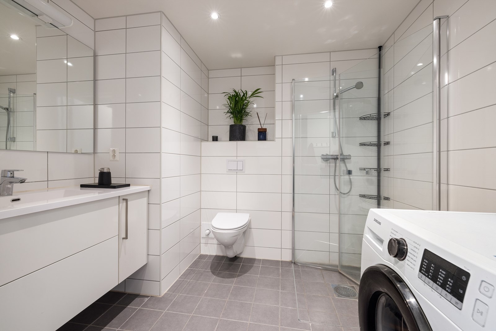 Badet er videre utstyrt med heldekkende servant, dusj m/innfelbbare glassdører, vegghengt wc, speil, downlightsbelysning og opplegg for vaskemaskin/tørketrommel Galleribilde