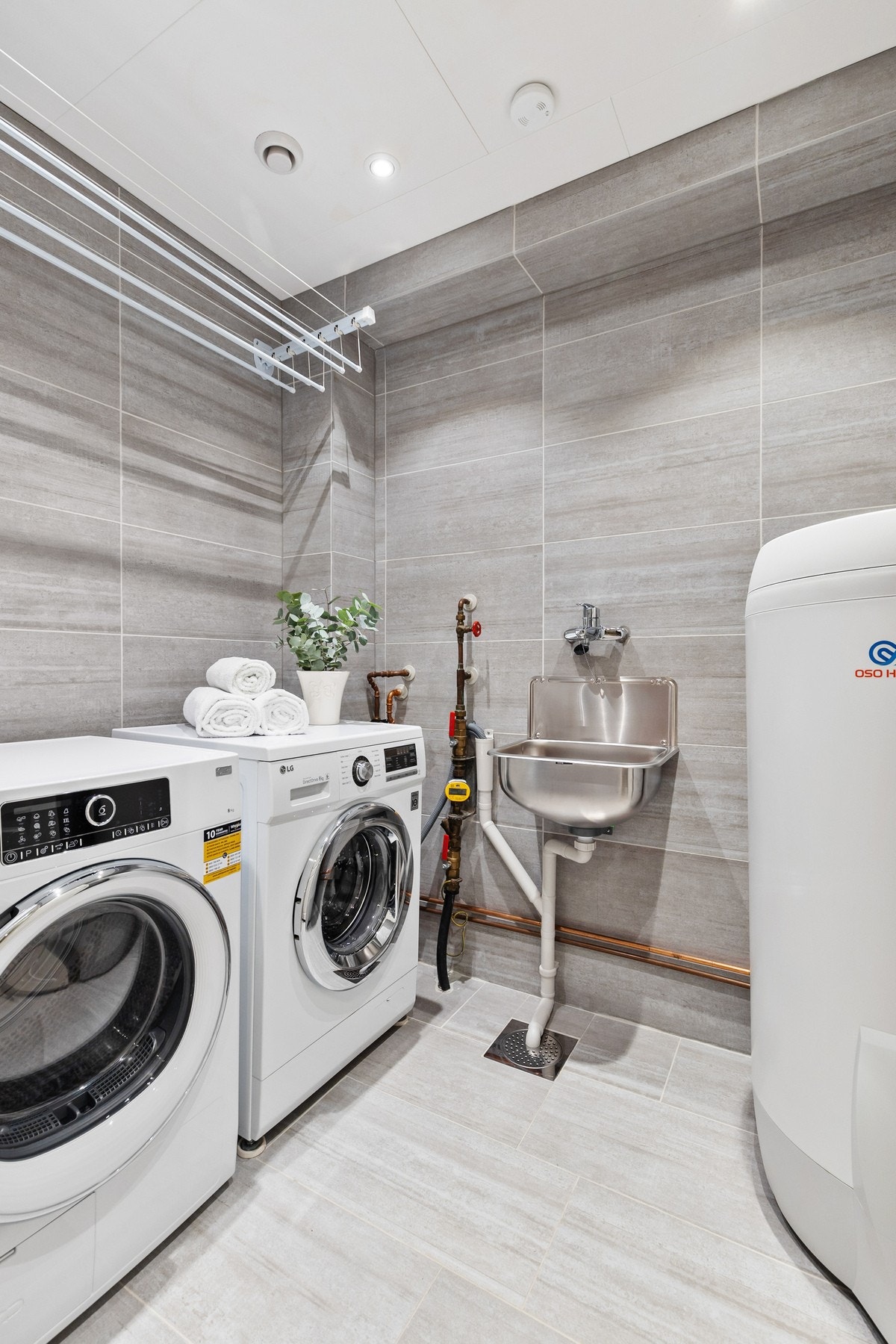 Praktisk, separat vaskerom med fliser på gulv og vegger samt gulvvarme og downlights. Rommet er utstyrt med vegghengt utslagsvask og opplegg for vaskemaskin Galleribilde