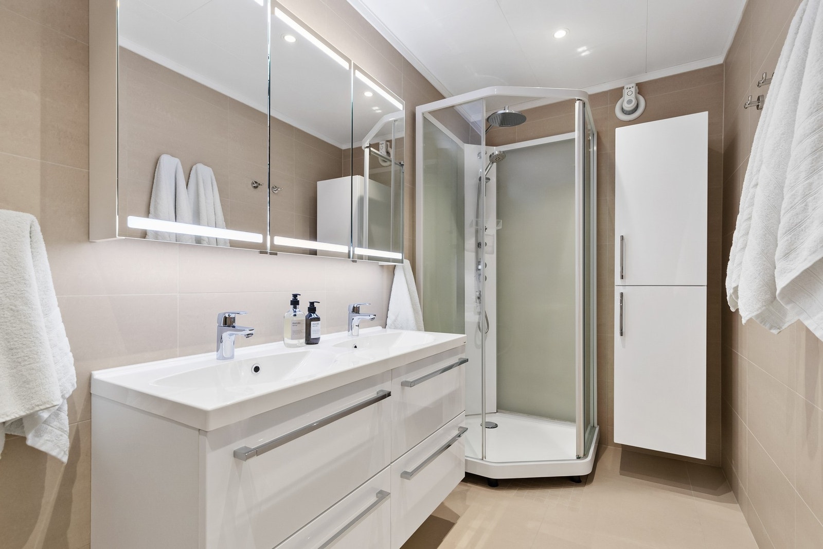 Rommet er innredet med servantinnredning med heldekkende dobbelservant, overskap, speil og dusjkabinett med regnfallsdusj Galleribilde