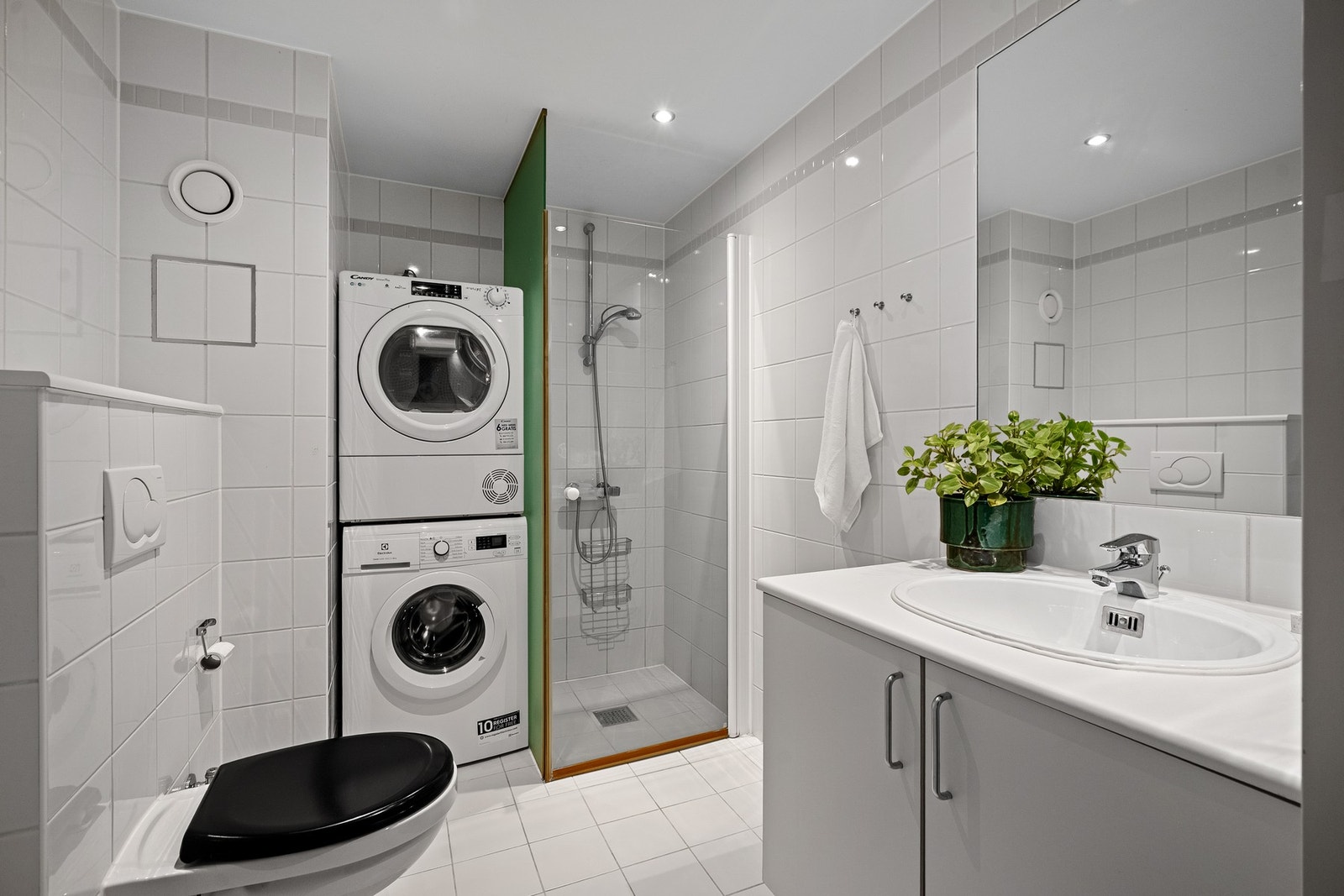 Tidløst, helfliset bad med romslig dusjhjørne og opplegg for vaskemaskin. Galleribilde