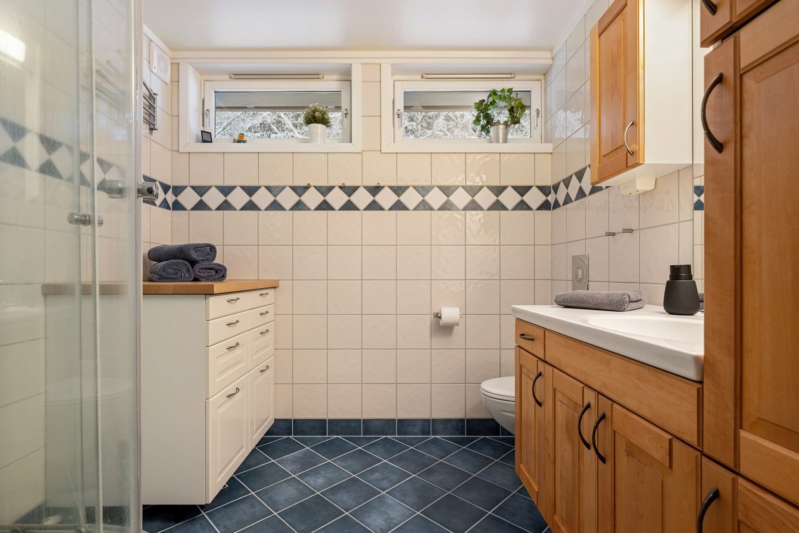 Romslig bad i andre etasje med fliser i behagelige toner og baderomsinnredning i varmt tre, samt dusjkabinett og veggmontert toalett. Galleribilde