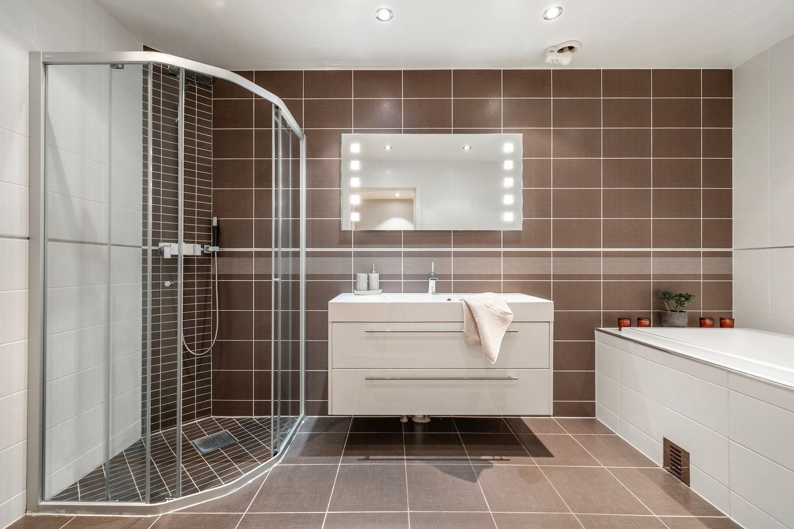 Badet er innredet med servantinnredning, speil på vegg over servant, vegghengt toalett, innmurt badekar og skjermet dusjhjørne. Galleribilde