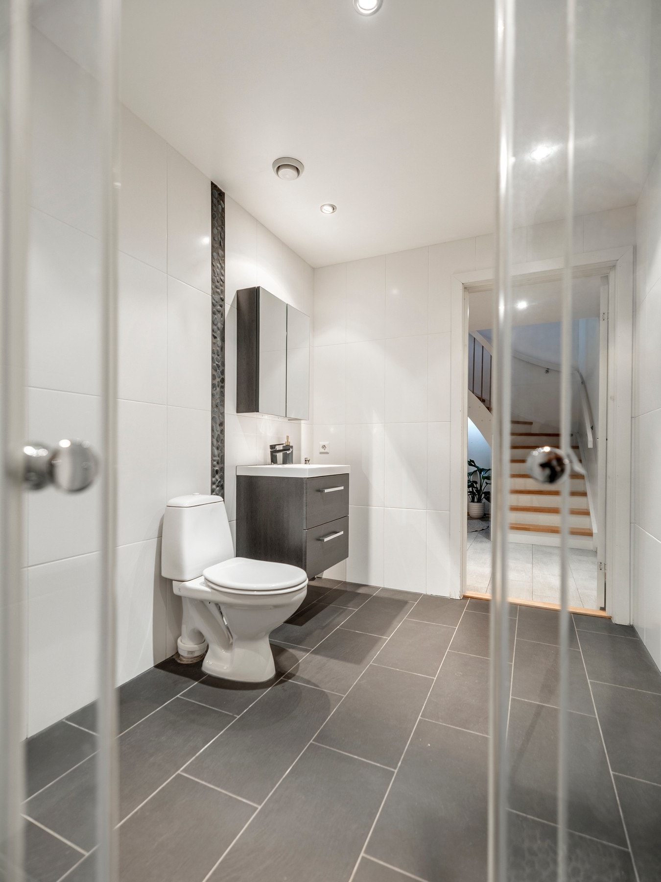 Badet er innredet med servantinnredning, speil i overskap på vegg over servant, toalett og skjermet dusjhjørne. Galleribilde