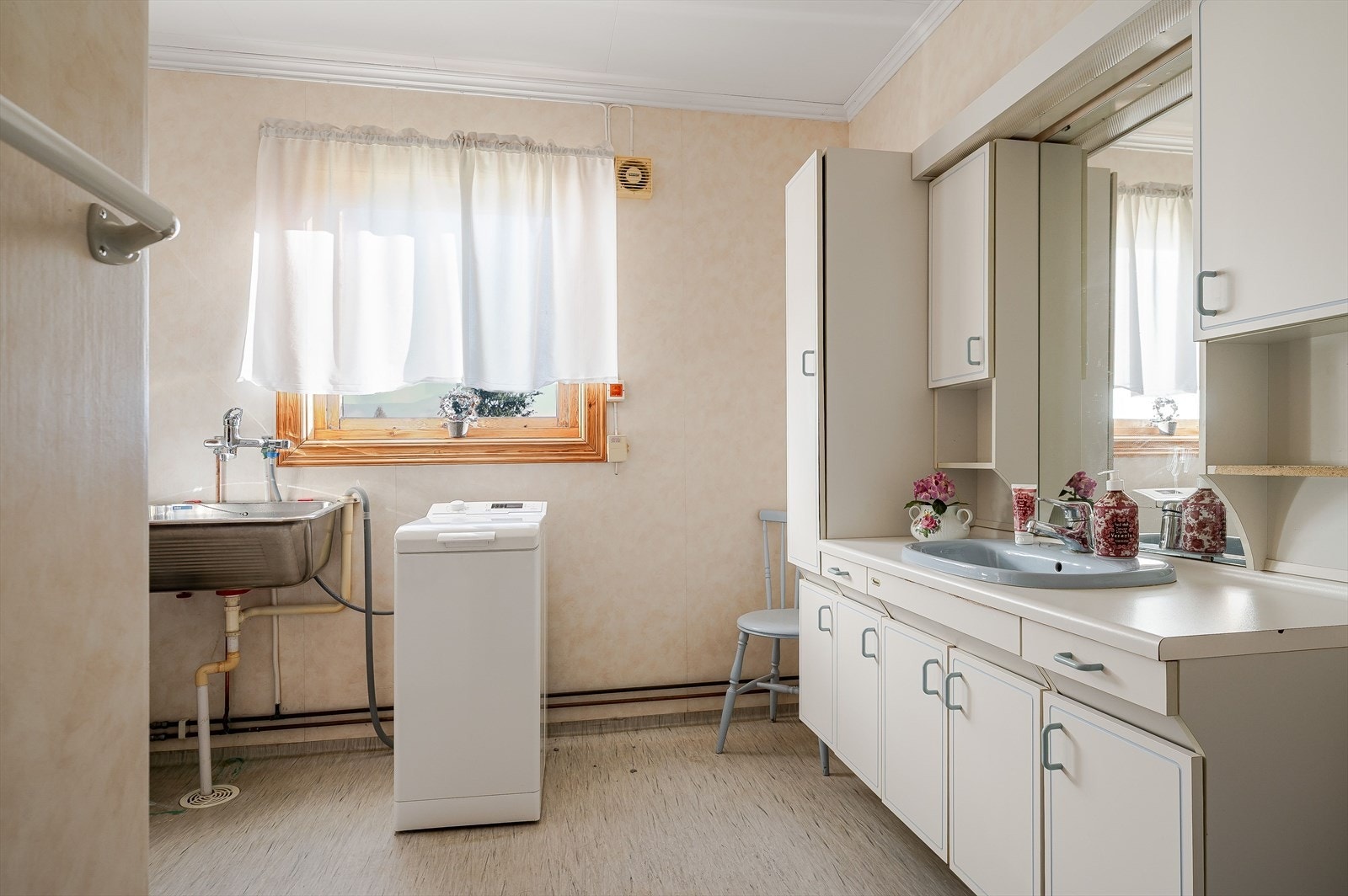 Lys baderomsinnredning med nedfelt servant, speil med belysning og vegghengte skap over. Baderommet er også utstyrt med badekar med vegghengt dusj, utslagsvask og opplegg for vaskemaskin. Galleribilde