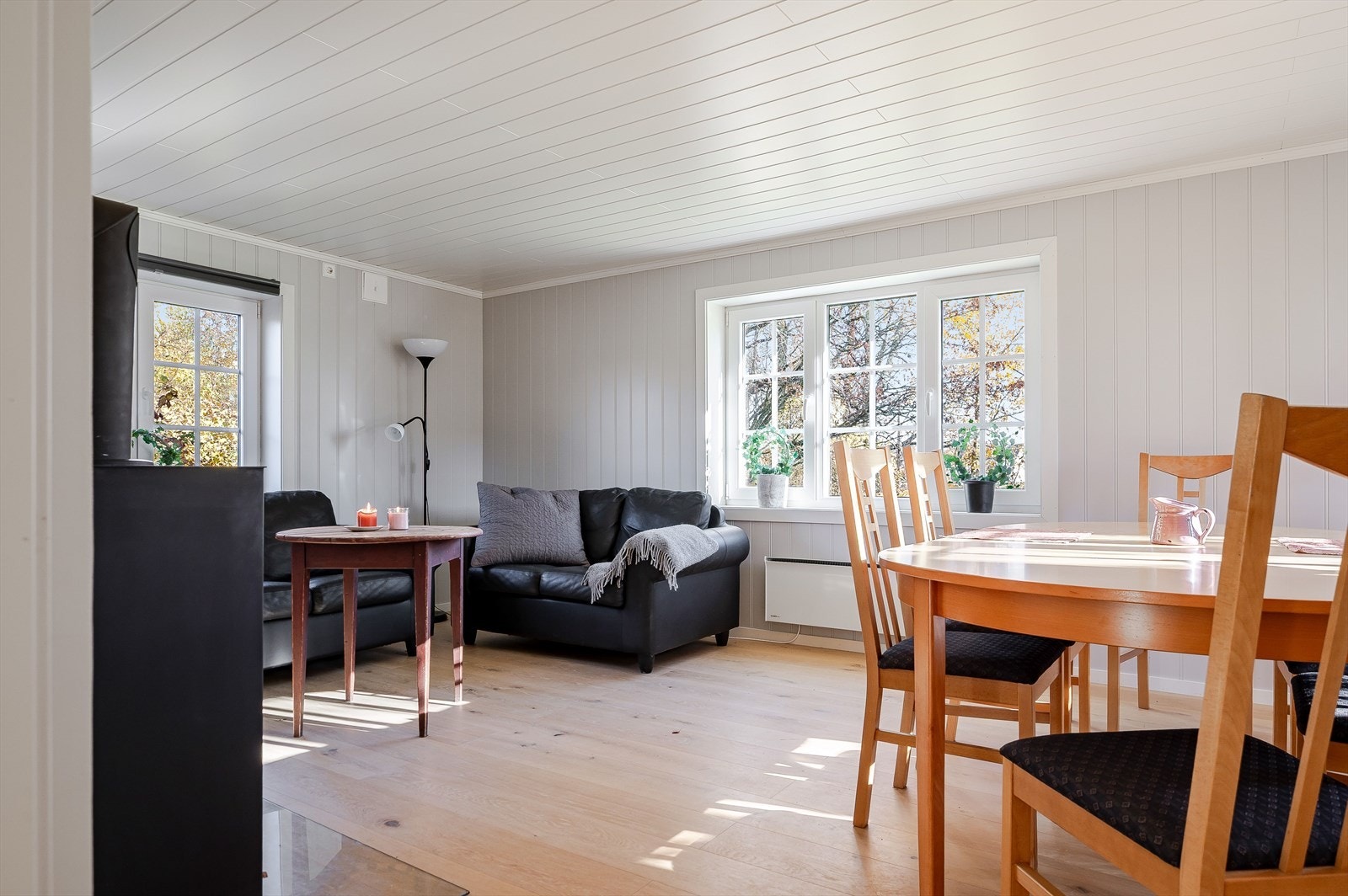 Lys og fin stue med enstavs parkett på gulv og lysmalte panelplater på veggene. Galleribilde