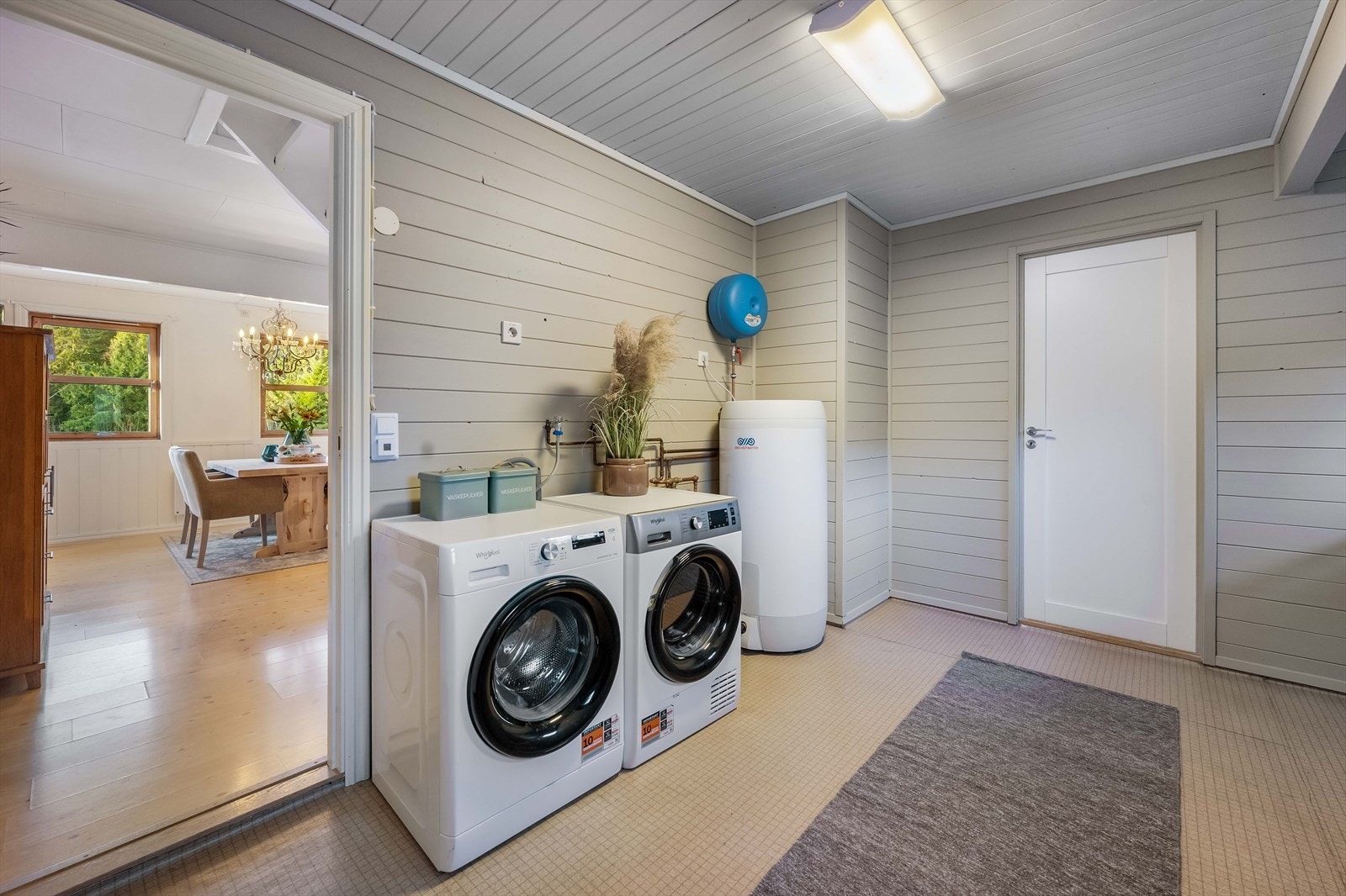 Eldre vaskerom med panel på vegger og belegg på gulv. Rommet har opplegg for vaskemaskin og varmtvannsbereder. Galleribilde