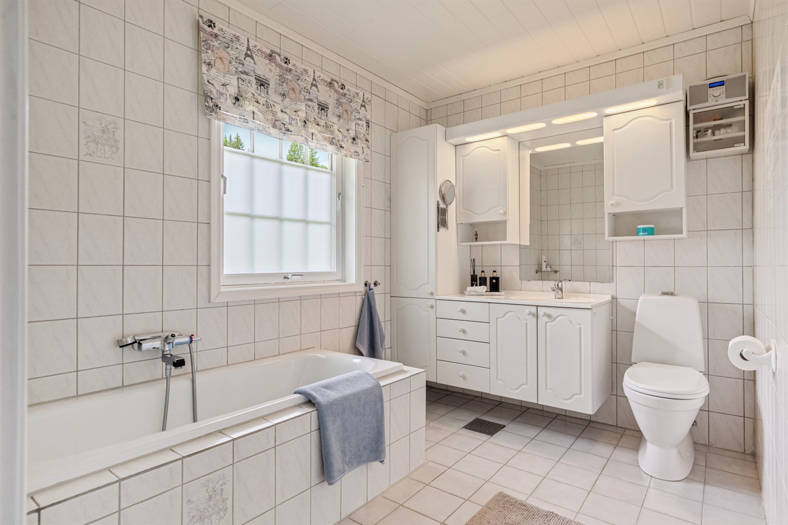 Flislagt bad med gulvvarme, servantskap med speil og lys, toalett og badekar. Galleribilde